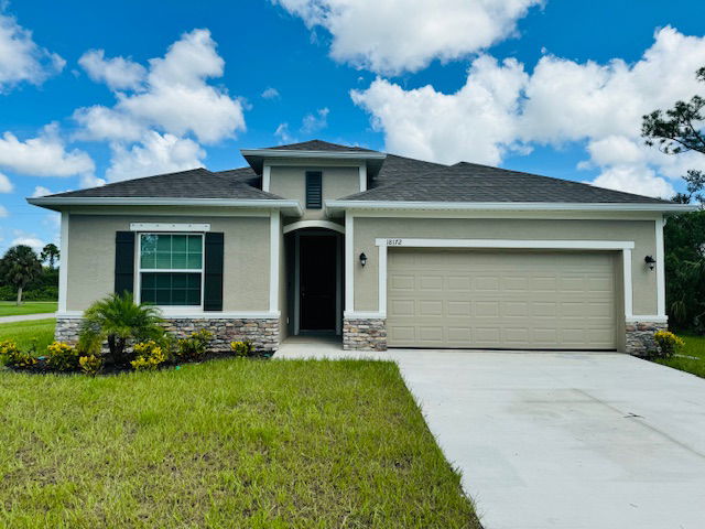 Modern single-story beige house with manicured lawn and two-car garage under a blue sky.