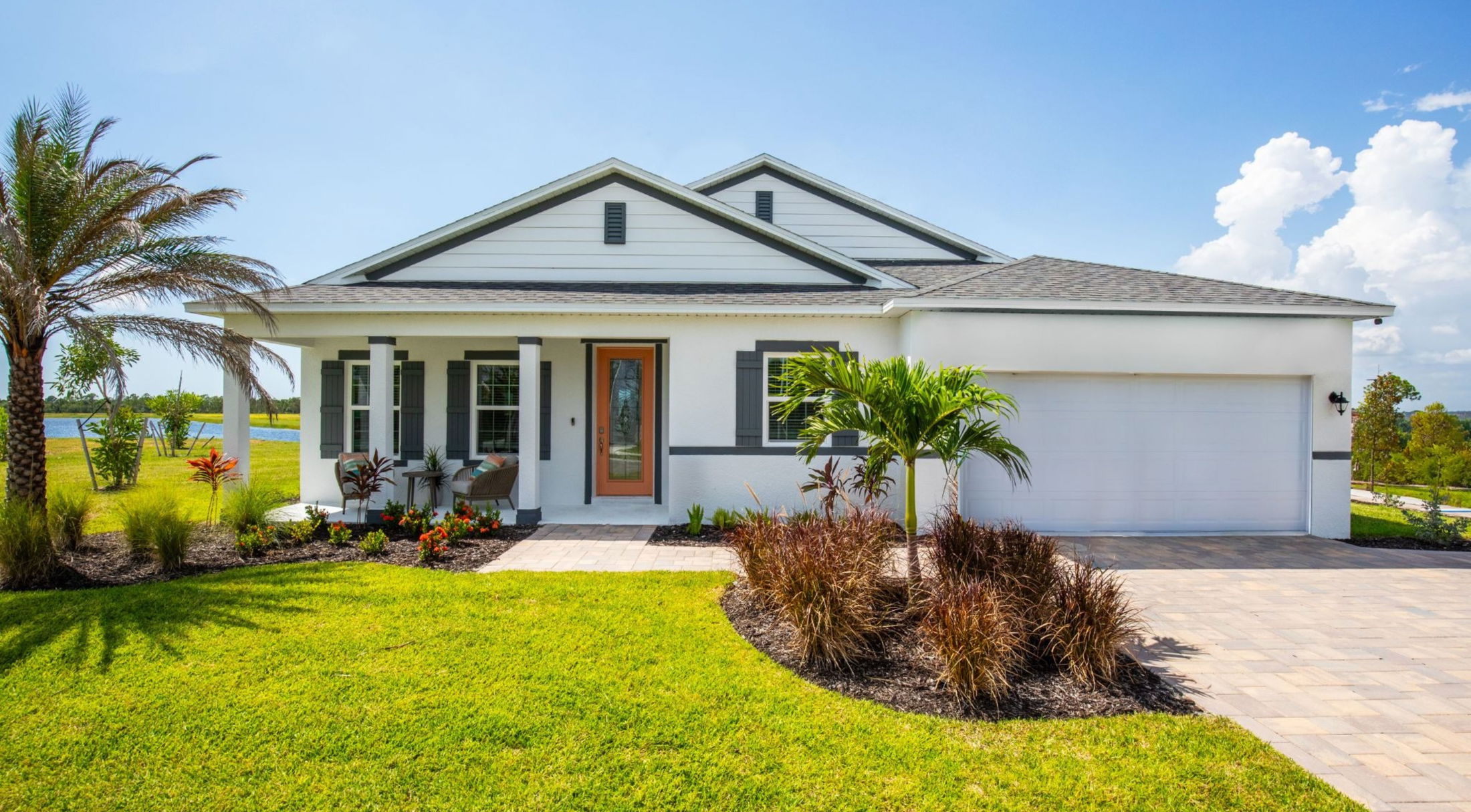 Modern single-family home with a front garden, palm trees, and a picturesque landscape under a clear blue sky.