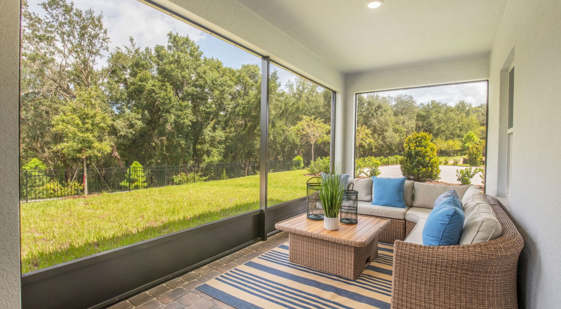 A cozy screened-in porch featuring a comfortable sectional sofa, a wooden coffee table, and a view of lush greenery.