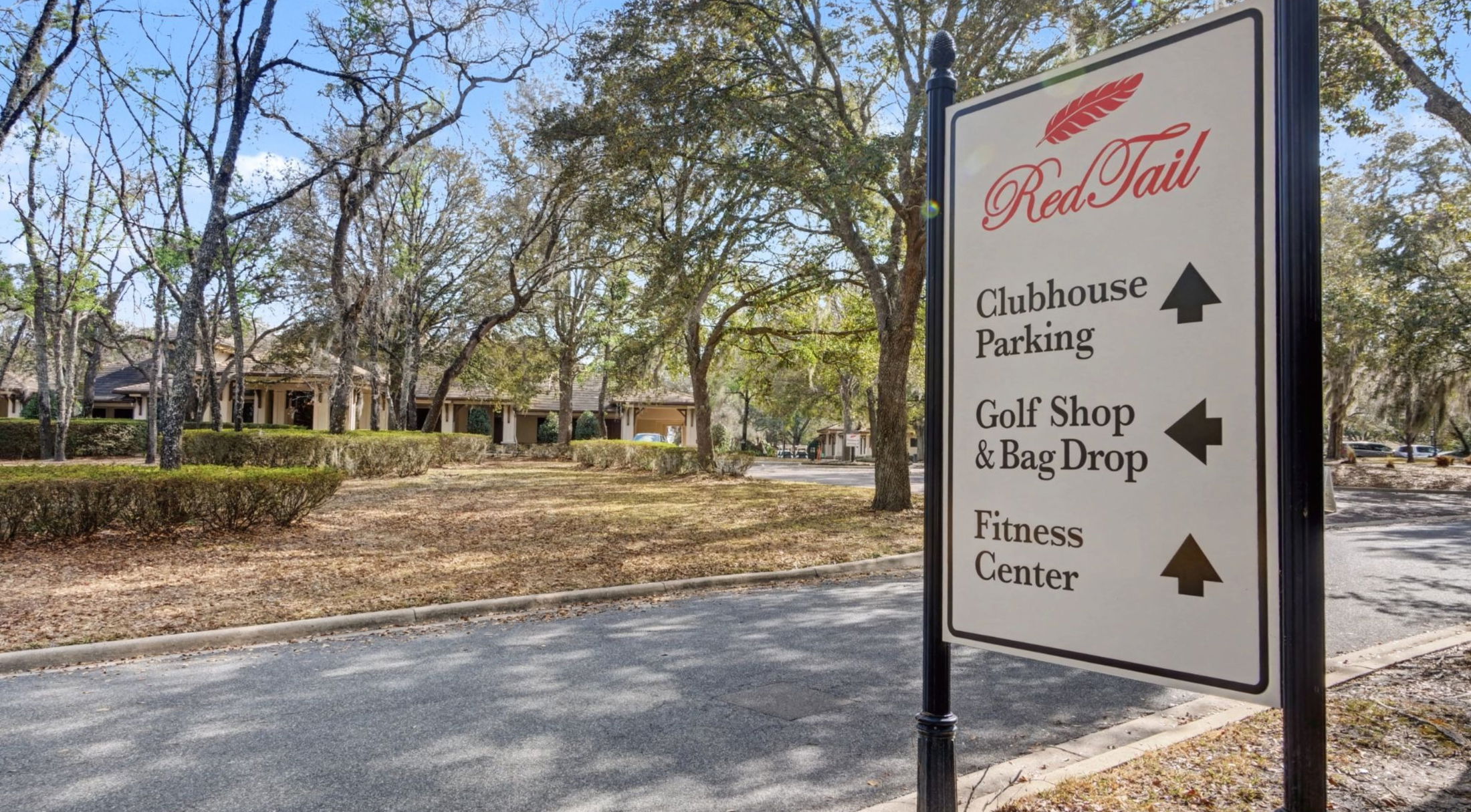 Directional sign at RedTail featuring directions to Clubhouse Parking, Golf Shop & Bag Drop, and Fitness Center, surrounded by trees and landscaping.