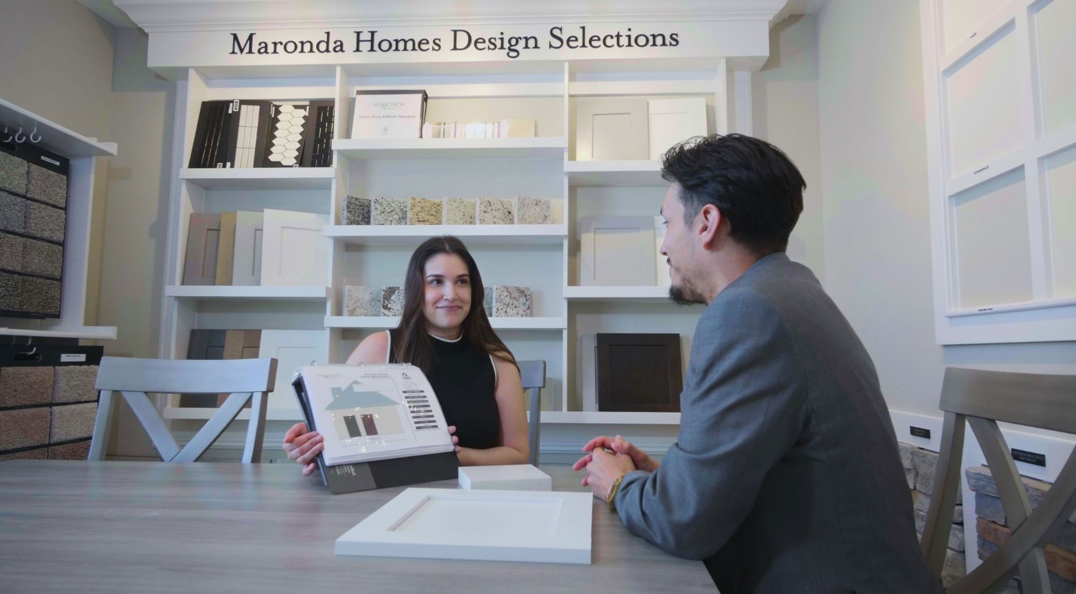 A woman and a man discuss design selections at Maronda Homes, showcasing various materials and color options on a table.