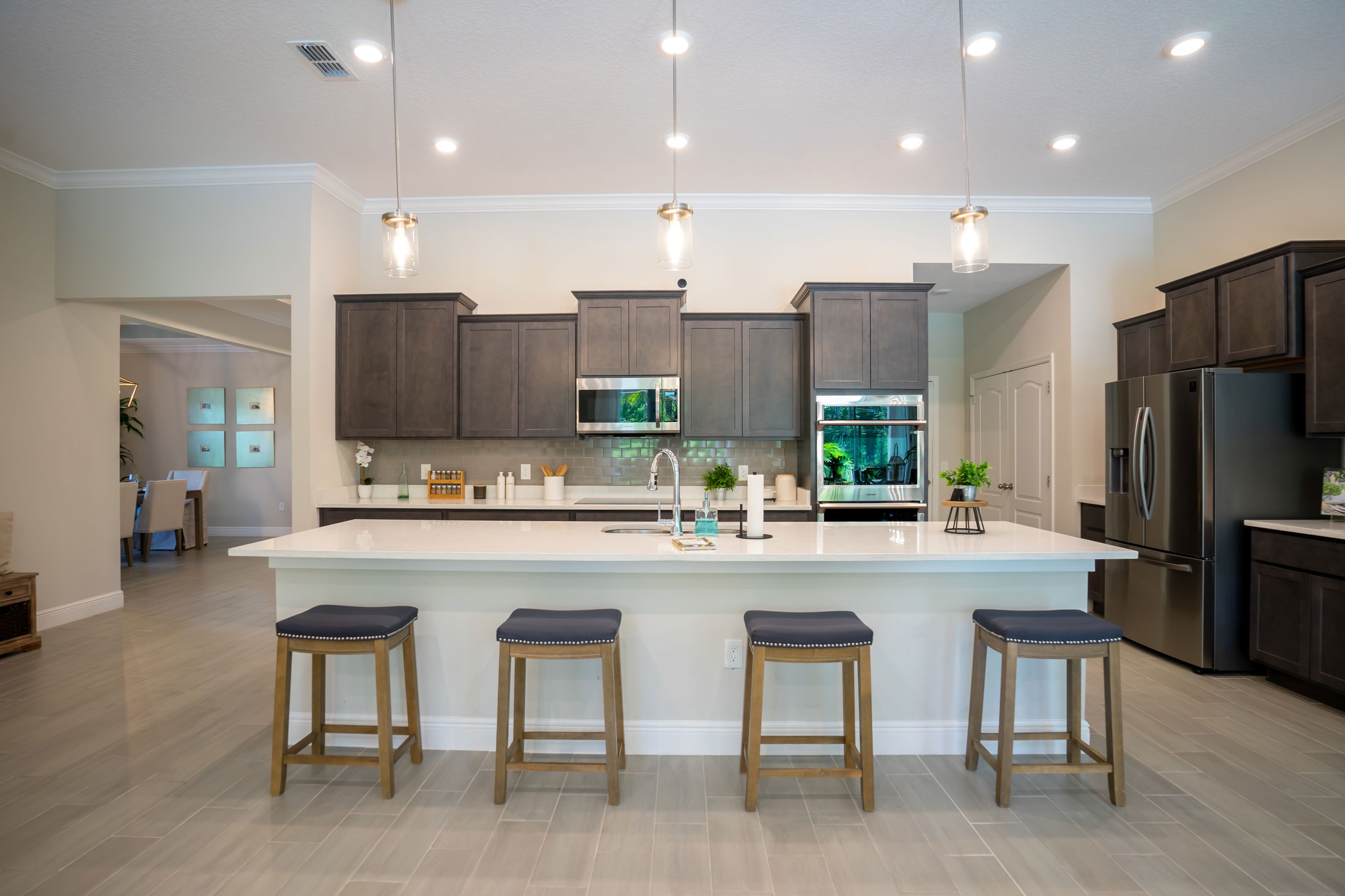 Modern kitchen with dark cabinets, stainless steel appliances, a large white island, and pendant lighting.