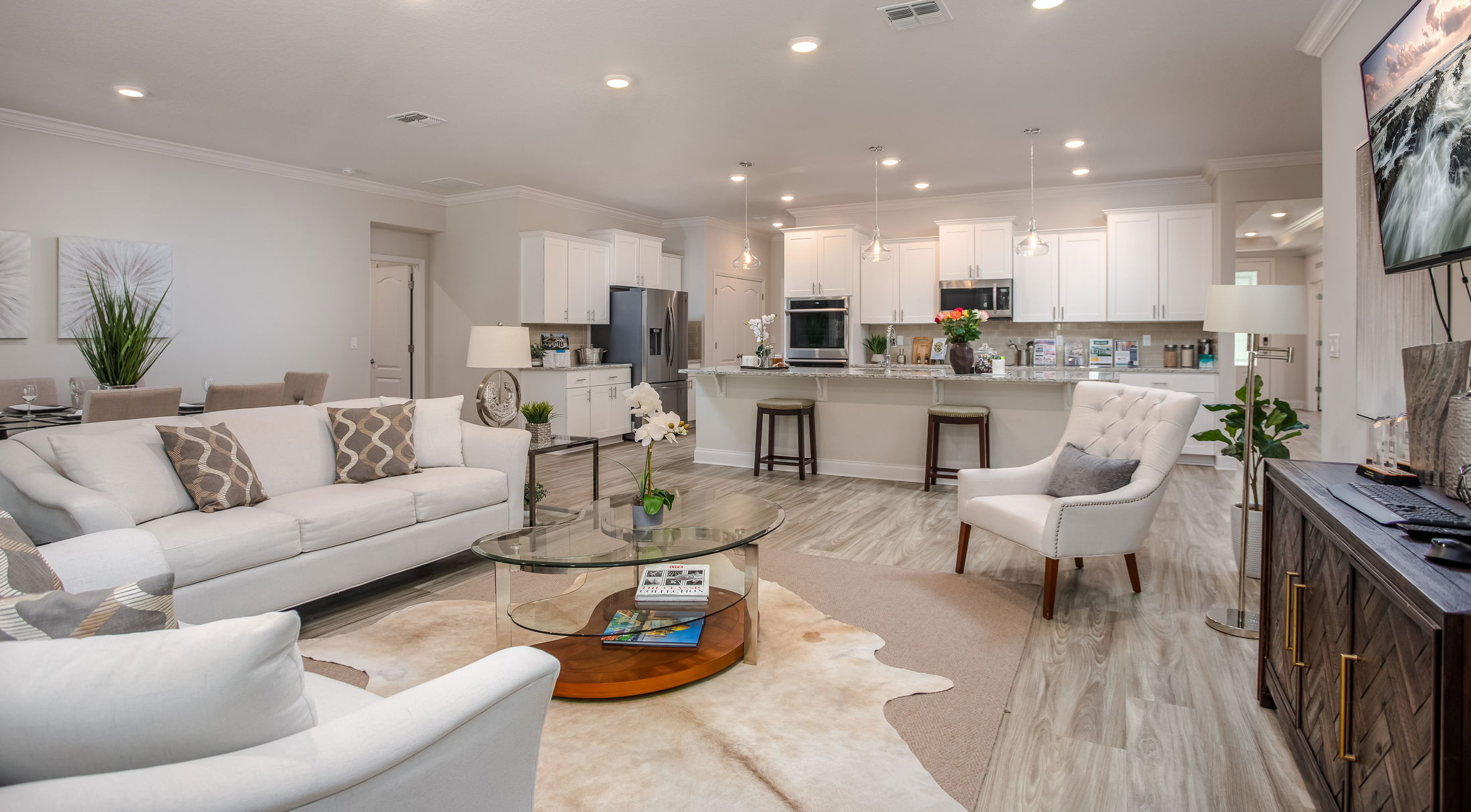 Modern open-concept living room and kitchen with white cabinetry, light wood flooring, and stylish neutral decor.
