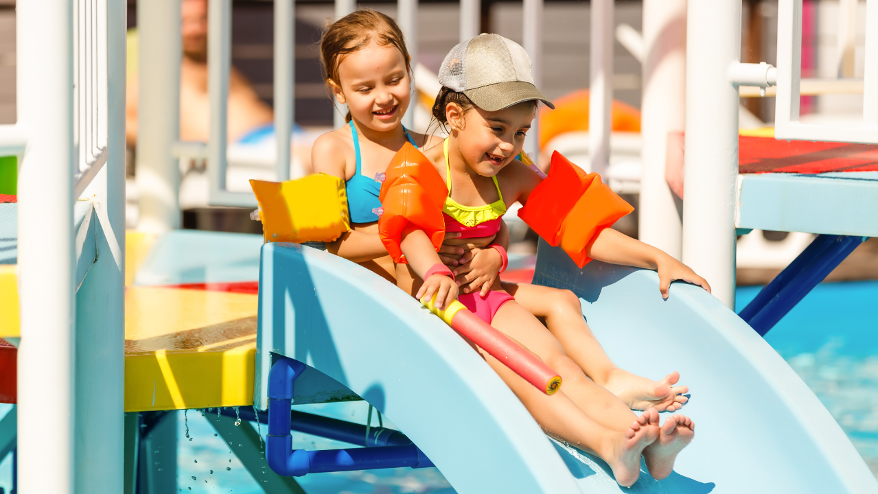 Two children wearing life jackets enjoy a fun slide at a colorful water playground.