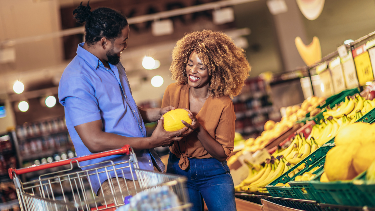 A happy couple shopping together in a grocery store, choosing fresh produce and holding a melon.
