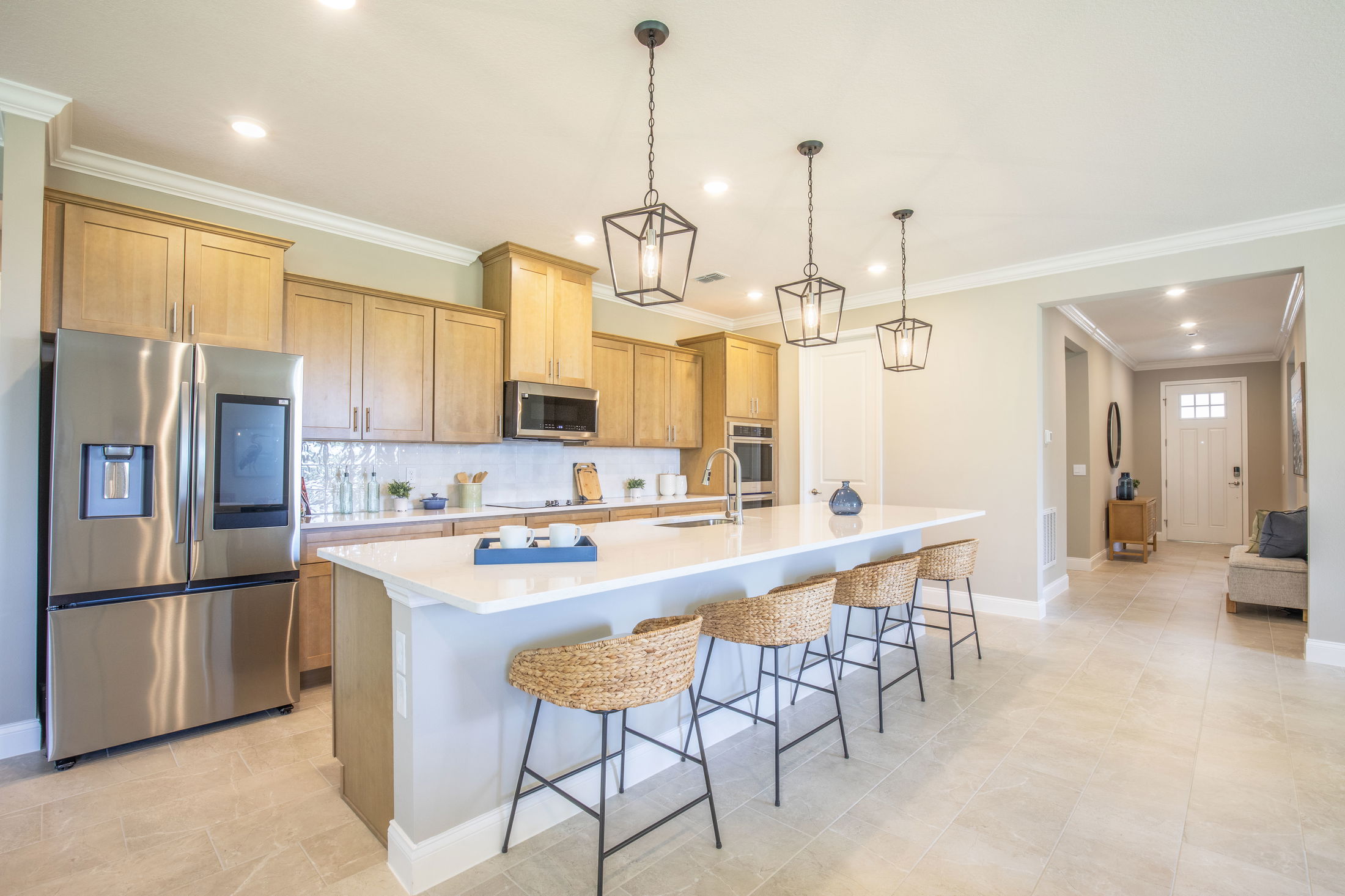 Modern kitchen with wooden cabinets, stainless steel appliances, and a large island with wicker bar stools and pendant lighting.