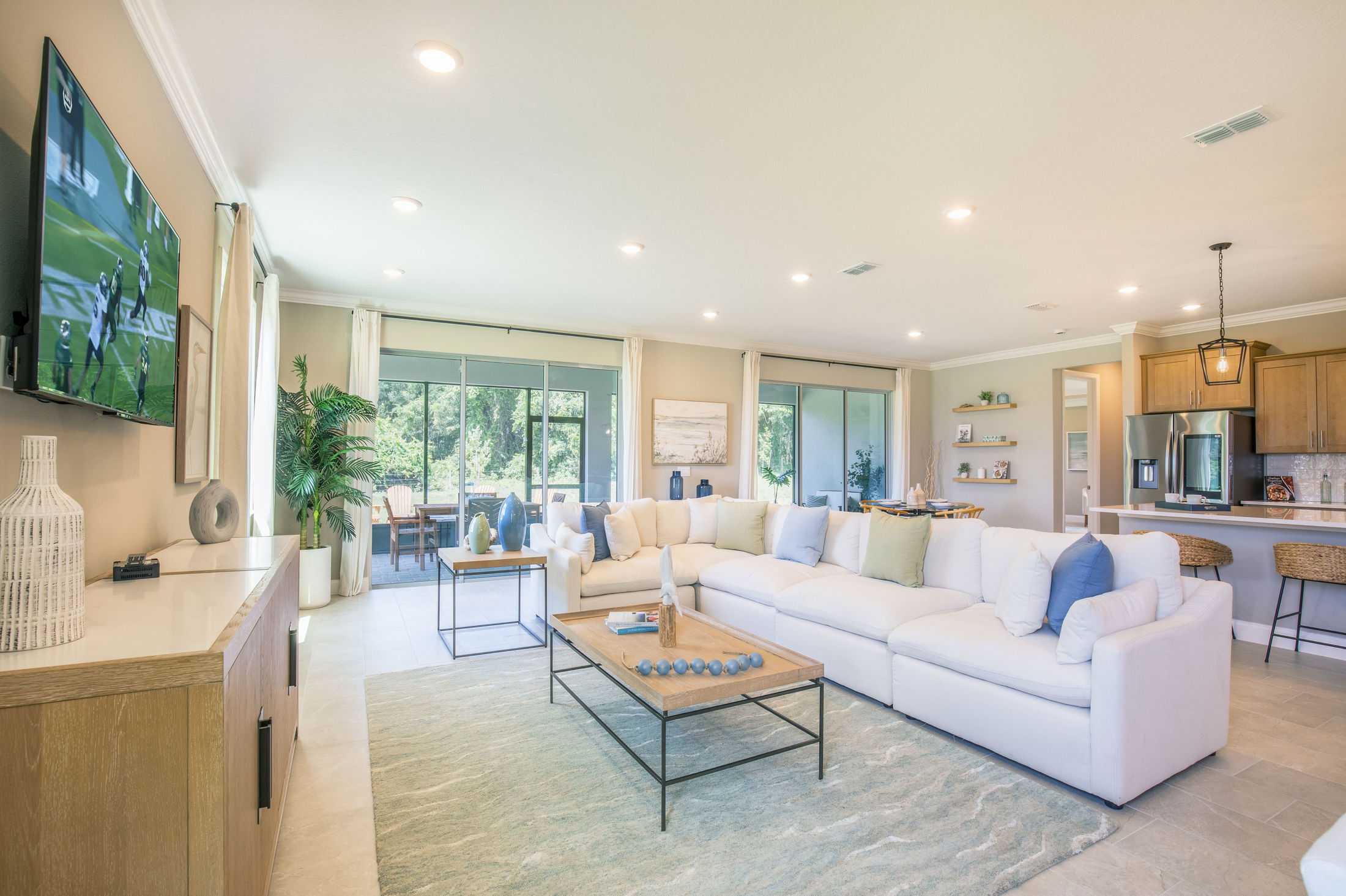 Modern living room with a large white sectional sofa, flat-screen TV, and open layout leading to the kitchen and dining area.