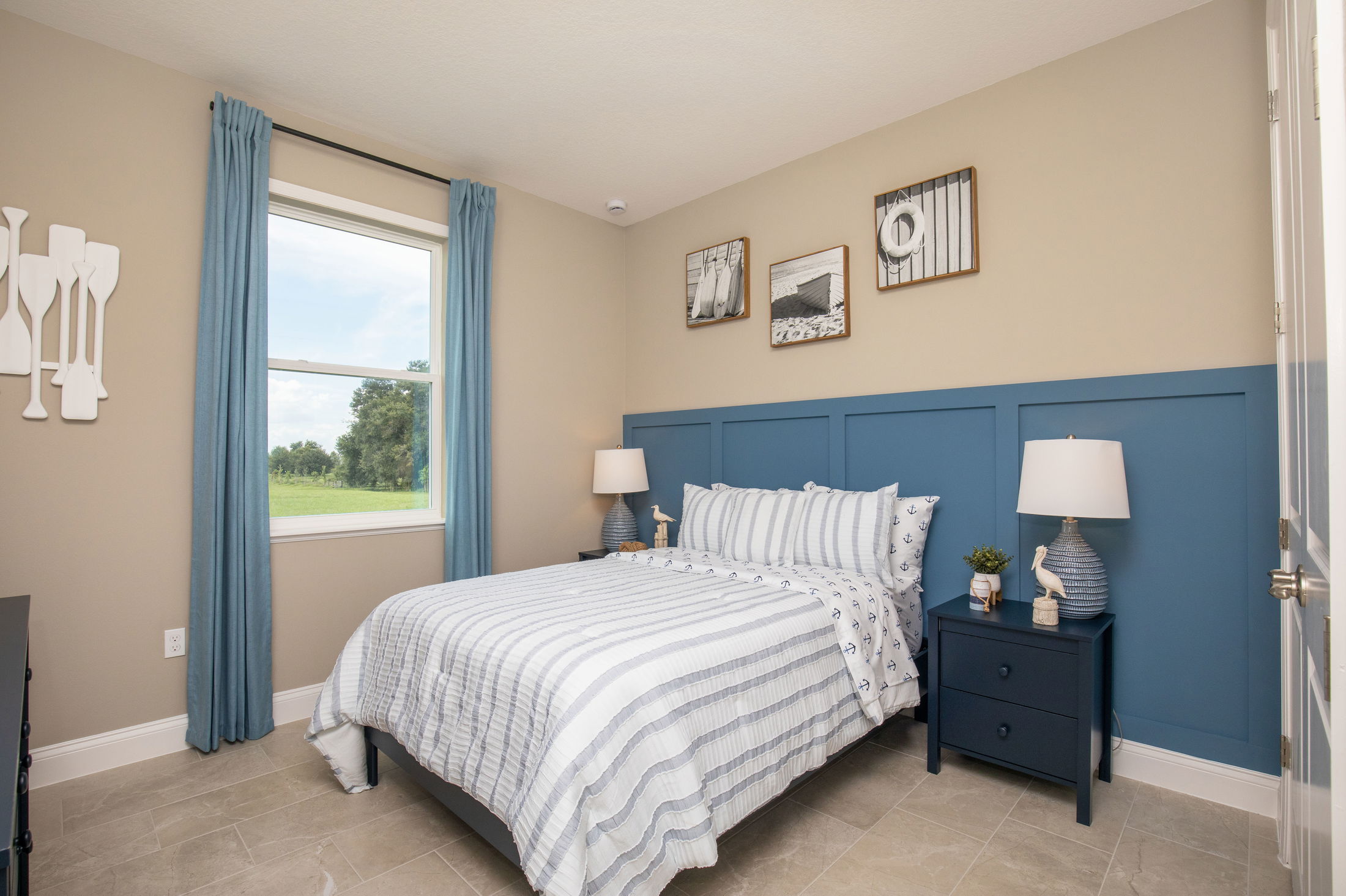 Modern bedroom with nautical-themed decor, featuring a blue paneled accent wall, striped bedding, and two bedside lamps.