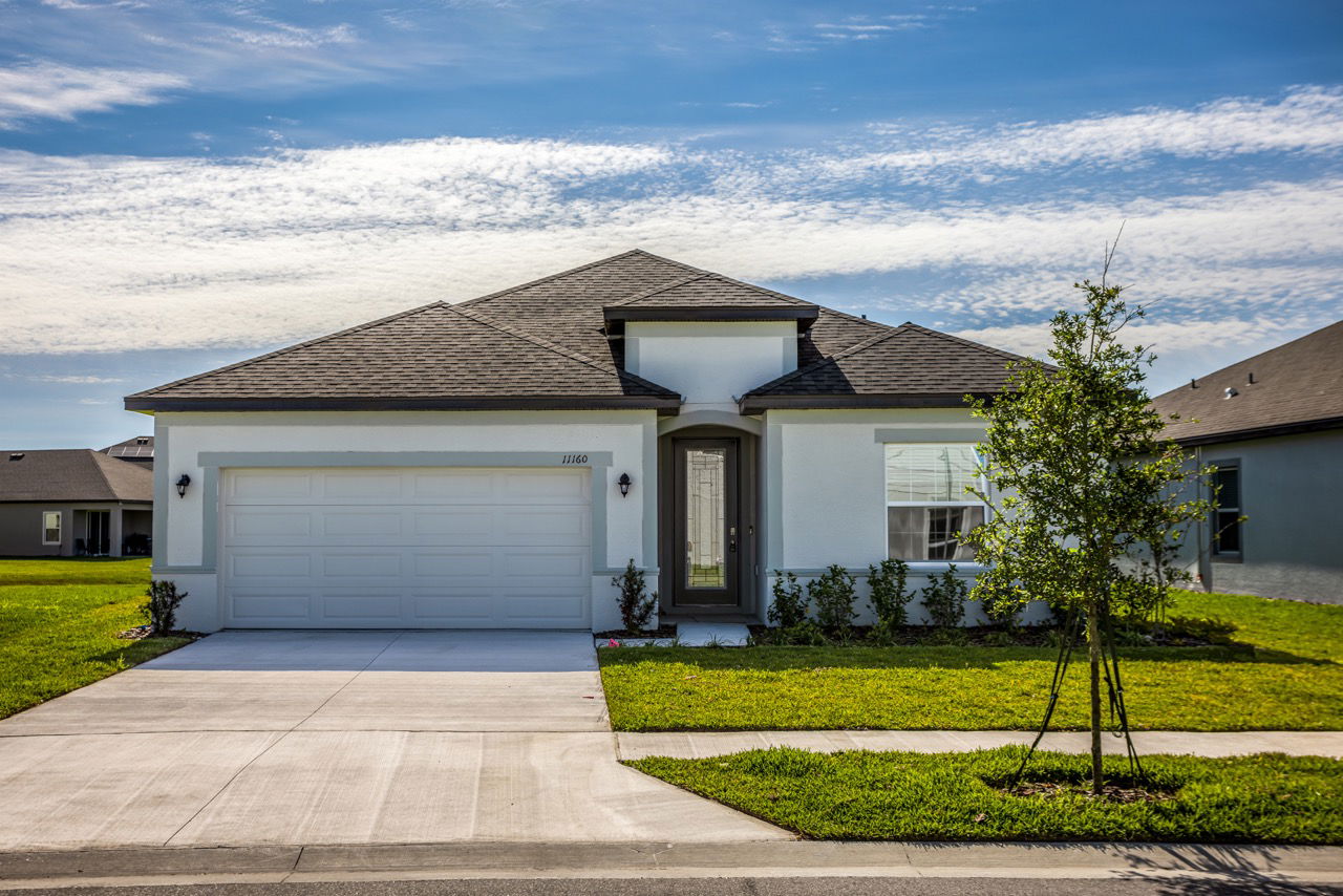 Modern single-story home with a grey shingled roof, white exterior, and well-maintained lawn under a clear blue sky.