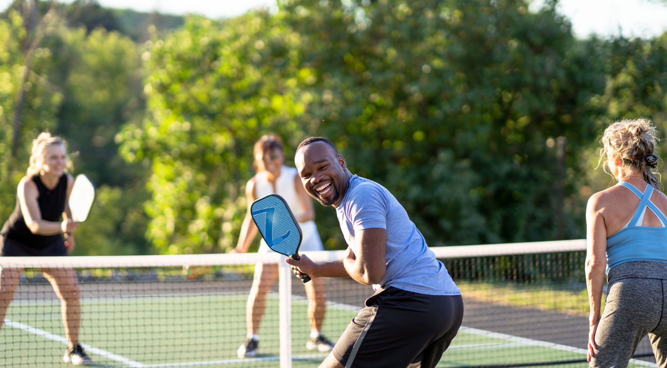 A group of four people enjoying a game of pickleball on an outdoor court surrounded by lush greenery.