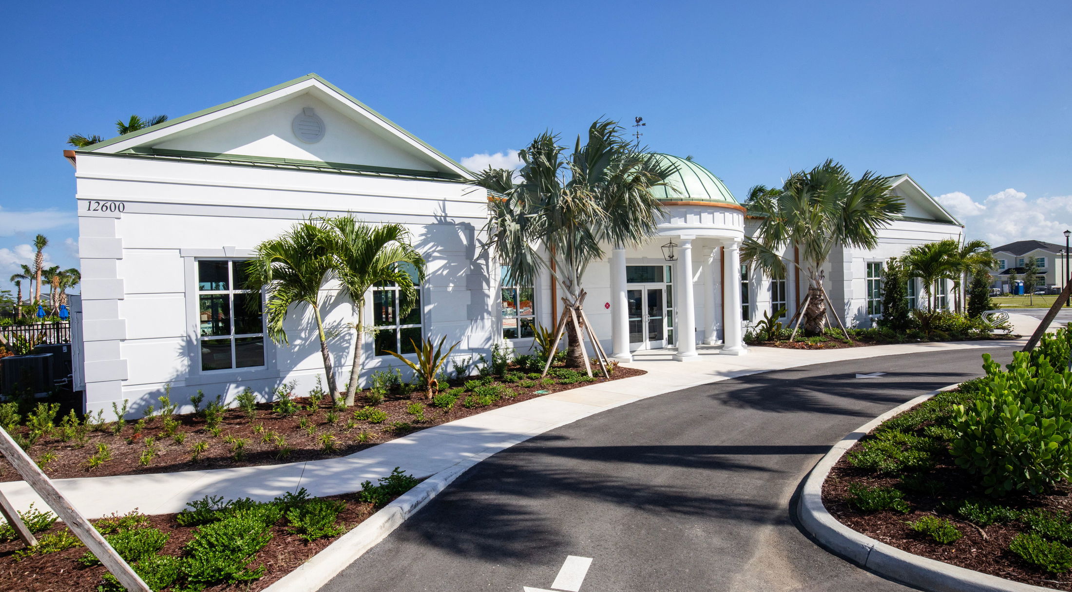 Elegant modern white building with palm trees and a circular driveway under a clear blue sky.