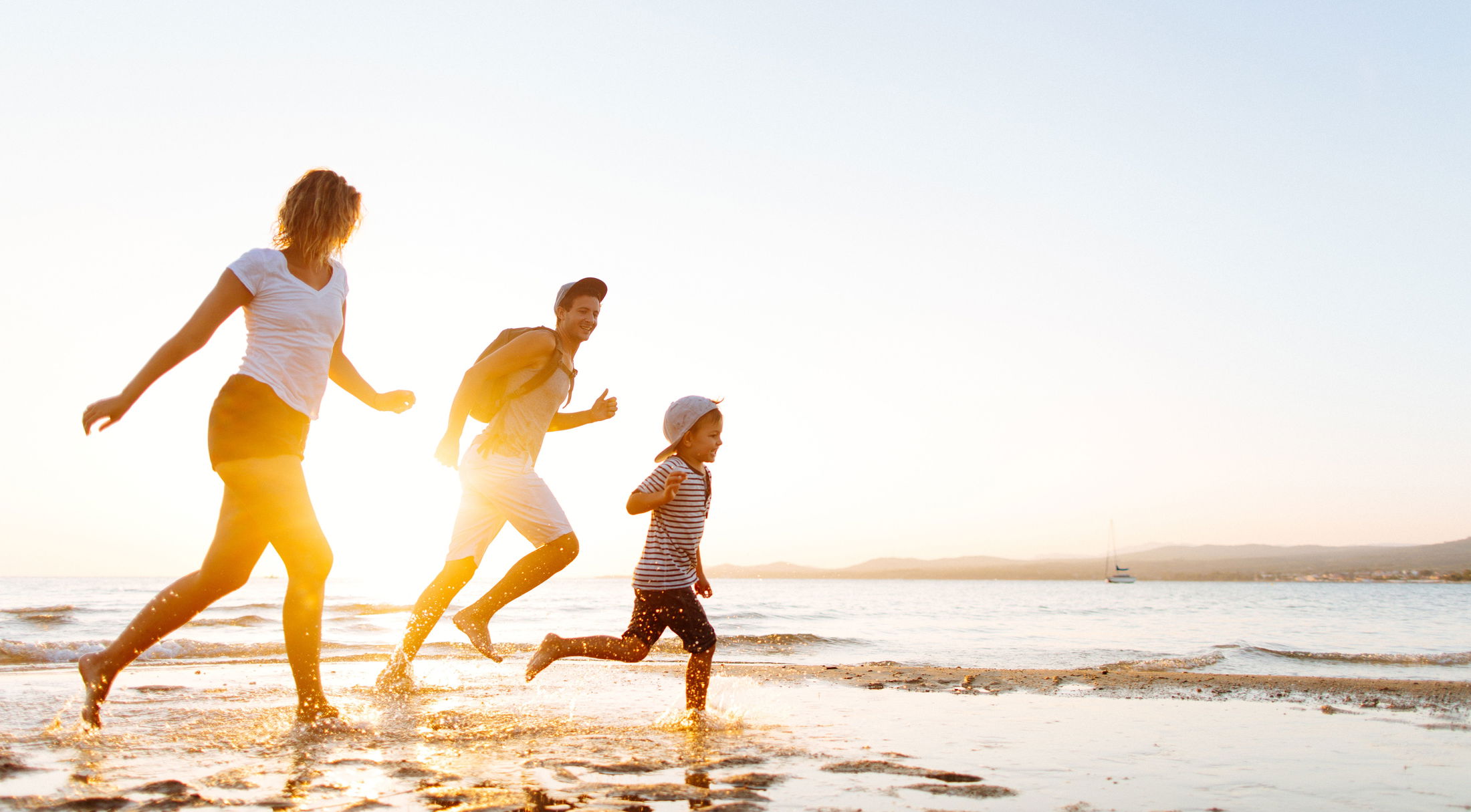 Family joyfully running on a sunlit beach during sunset, enjoying a summer vacation by the sea.