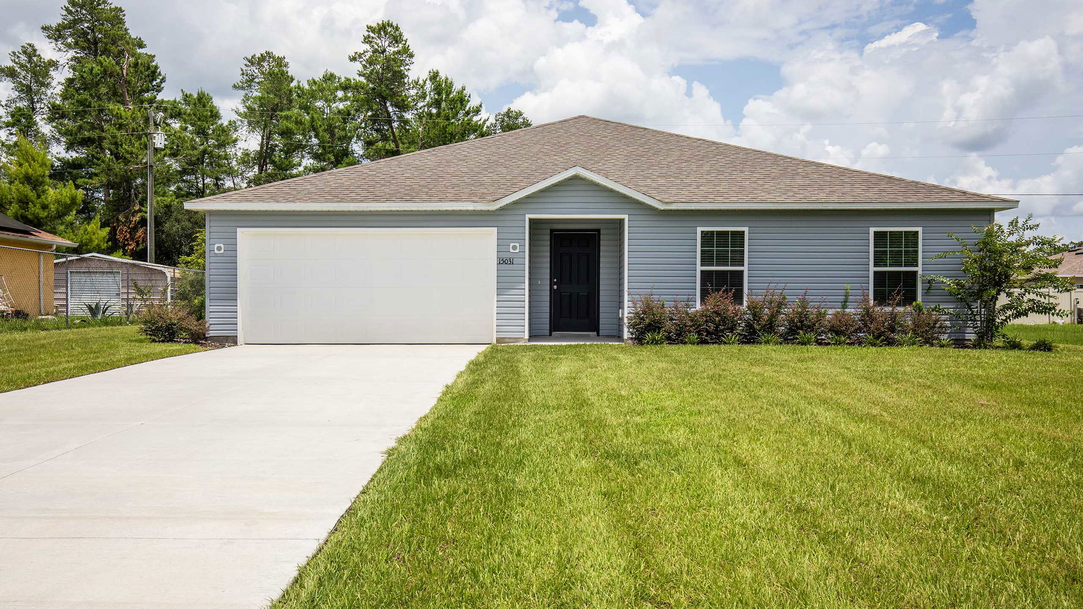 Single-story blue house with a neatly manicured lawn and attached garage in a suburban neighborhood.