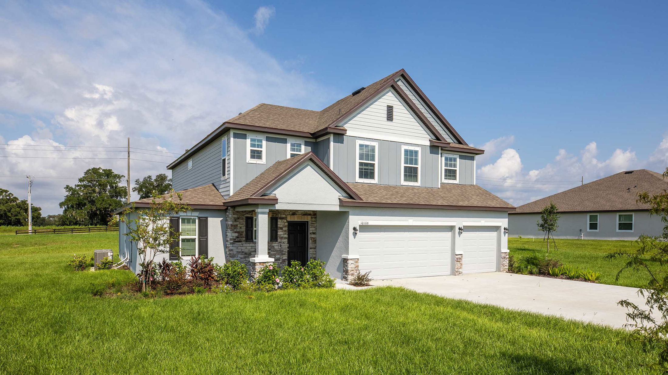 Modern two-story suburban house with a large driveway and well-maintained lawn under a clear blue sky.