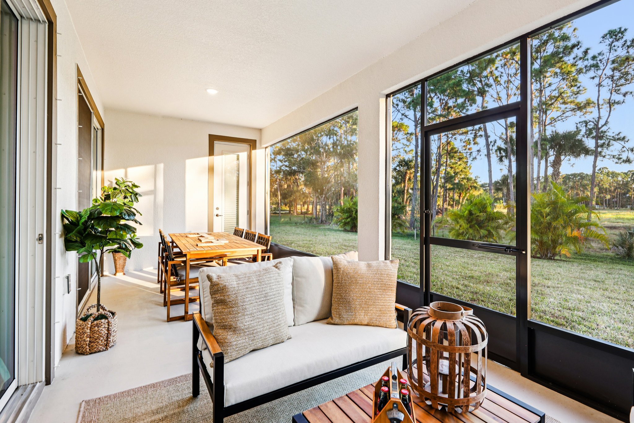 Bright and airy screen porch with cozy seating, a wooden dining table, and lush garden views.
