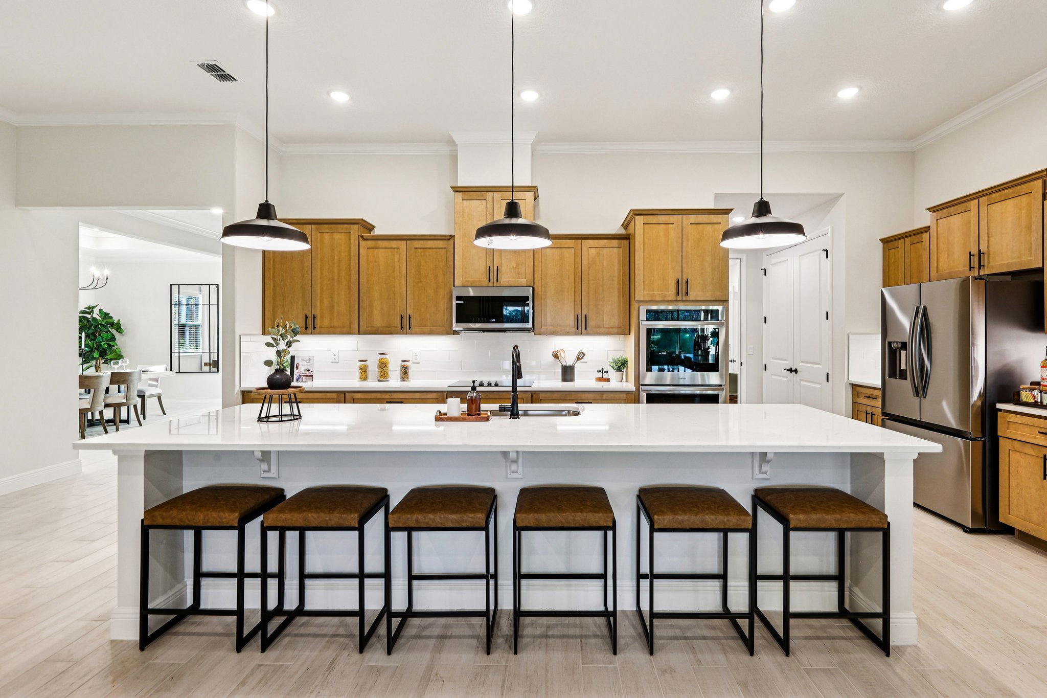 Modern kitchen with wooden cabinets, a spacious white island with bar stools, stainless steel appliances, and pendant lighting.