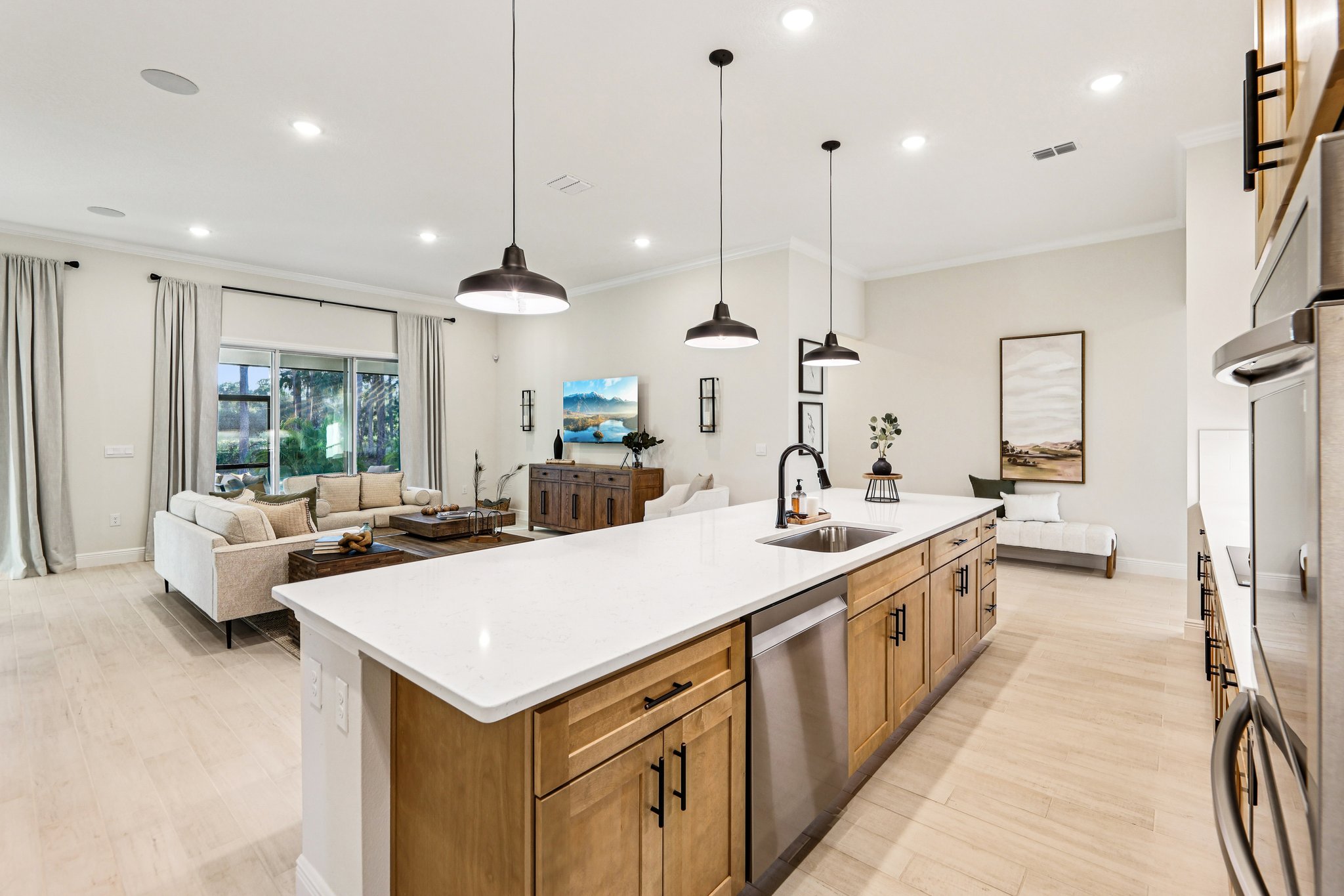 Modern open-concept kitchen and living room with wooden cabinetry, pendant lighting, and neutral furnishings.