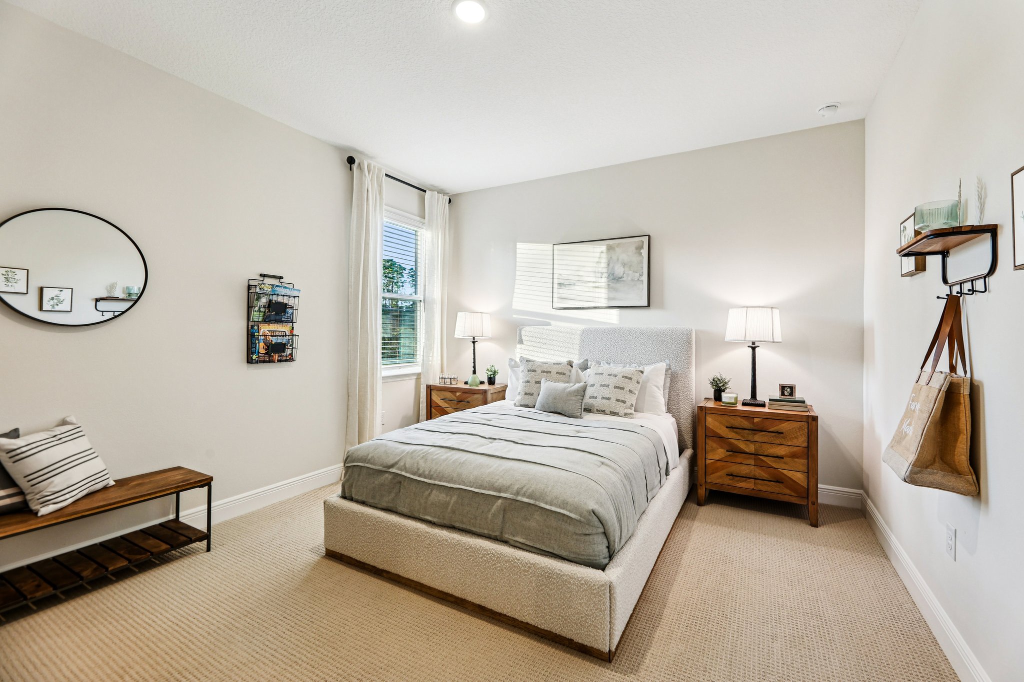 Modern bedroom with stylish decor, featuring a bed with gray bedding, wooden nightstands, and a round mirror on a beige wall.
