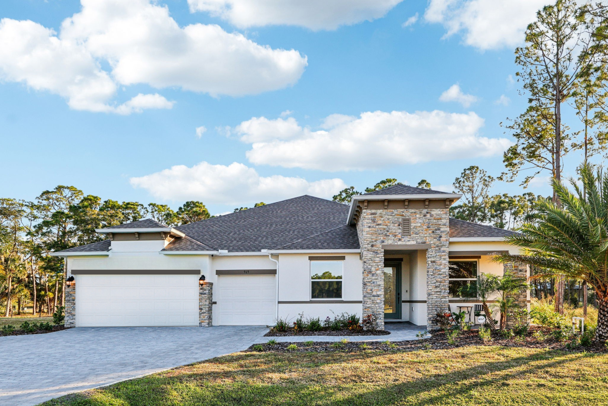 Modern one-story house with stone facade and a three-car garage set against a clear blue sky.