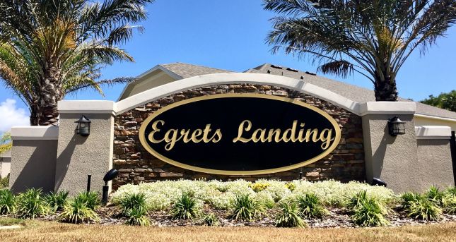 Alt tag: "Entrance sign for Egrets Landing community, featuring landscaped greenery and palm trees."