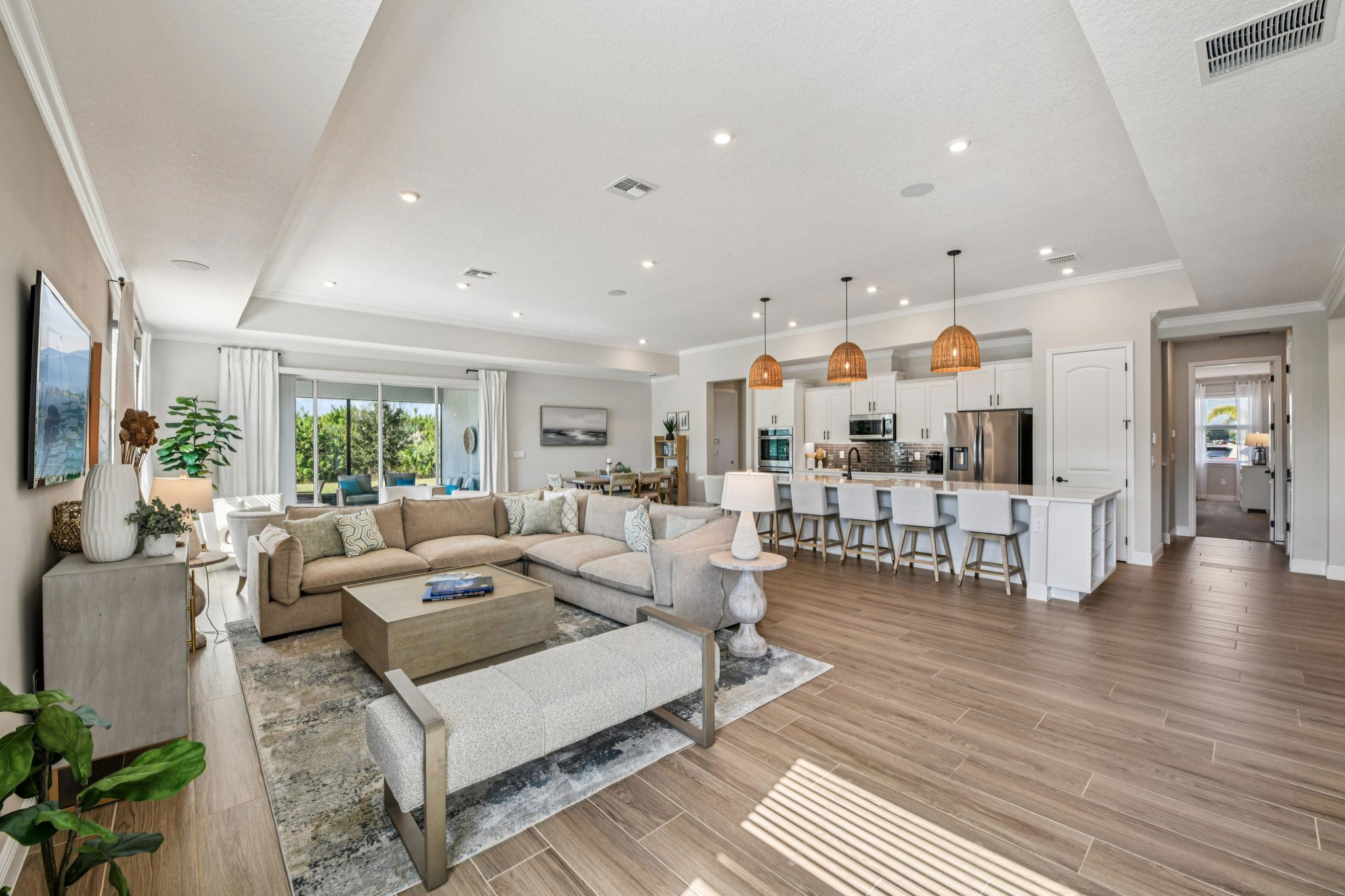 Modern open-concept living room and kitchen with neutral tones, featuring a large sectional sofa, pendant lighting, and sleek kitchen island seating.