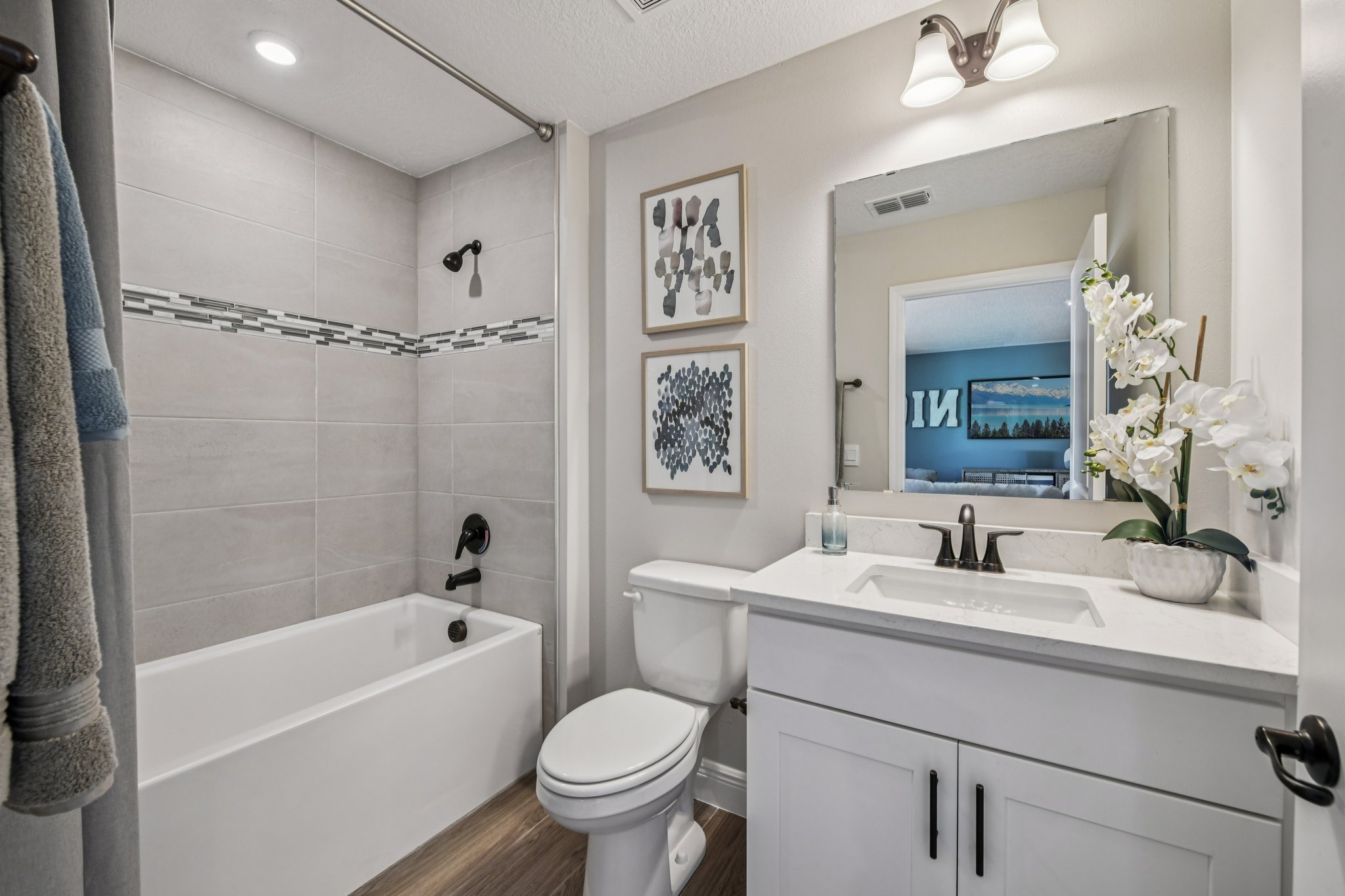 Modern bathroom with a white bathtub, stylish tile backsplash, white vanity with marble countertop, and decorative wall art.