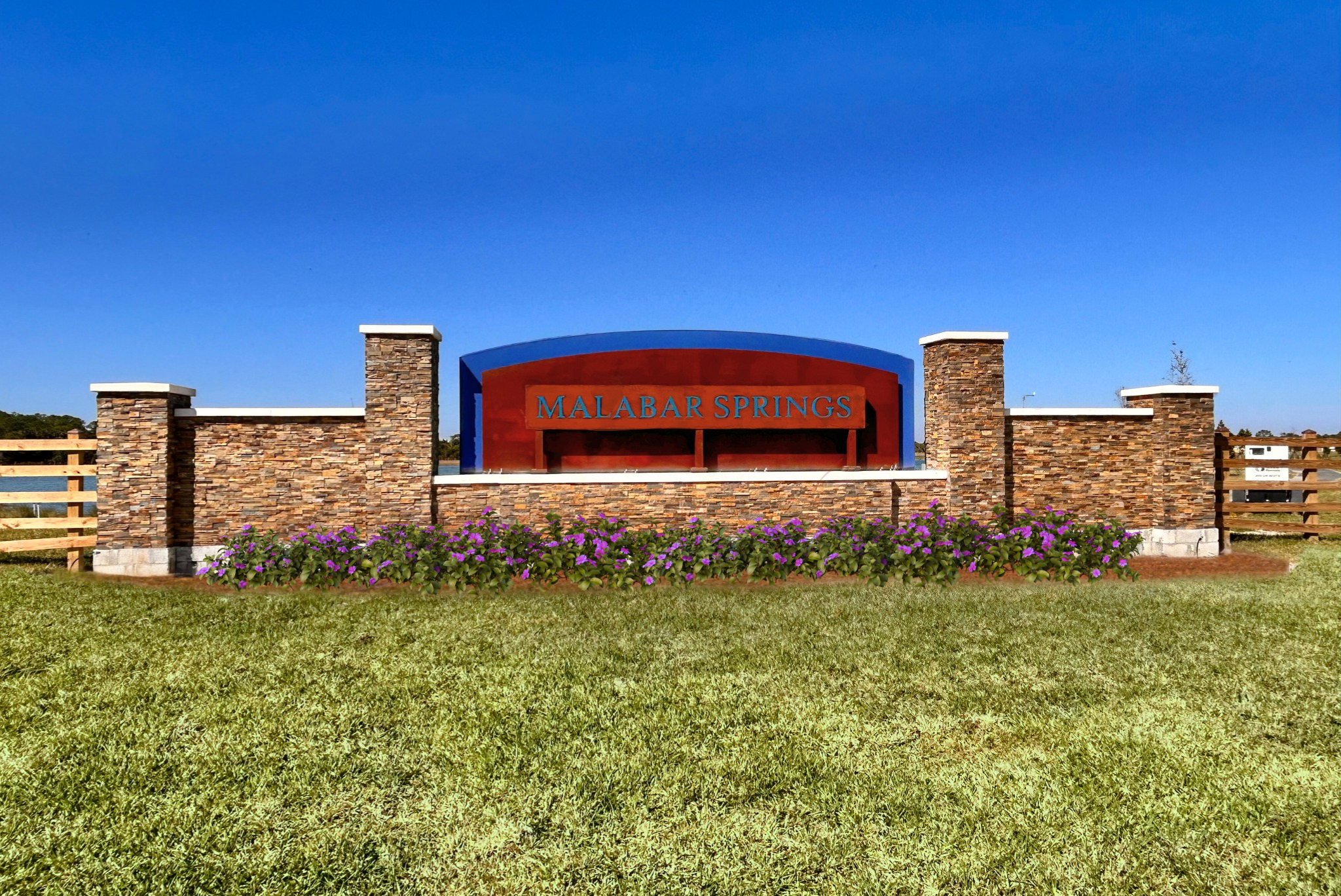 Signage for Malabar Springs surrounded by vibrant flowers and green grass under a clear blue sky.