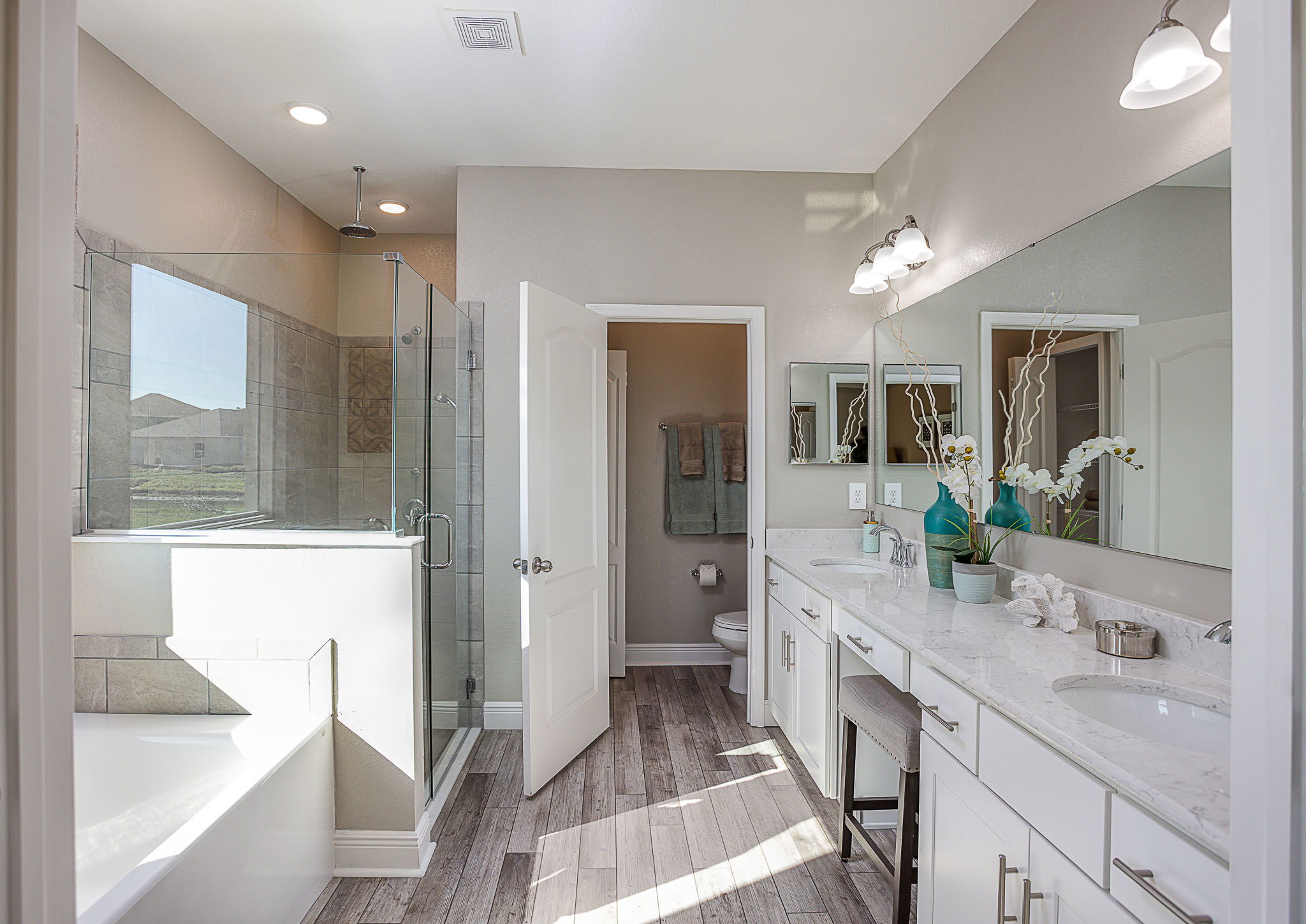 Modern bathroom featuring a glass shower, soaking tub, dual-sink vanity, and large mirror with elegant decor.