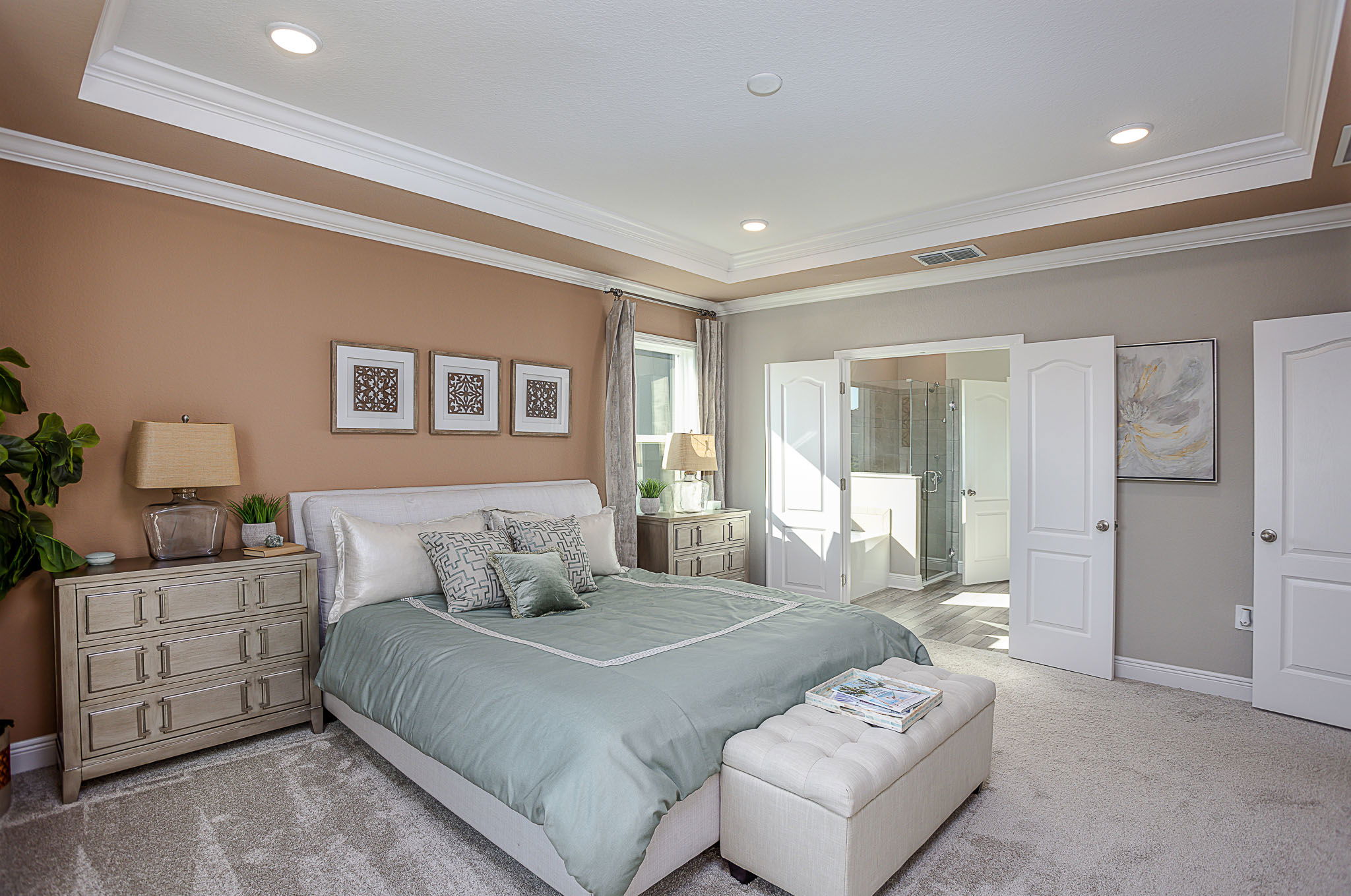 Elegant master bedroom with earth-toned walls, featuring a large bed with green bedding, two nightstands, and an en suite bathroom.