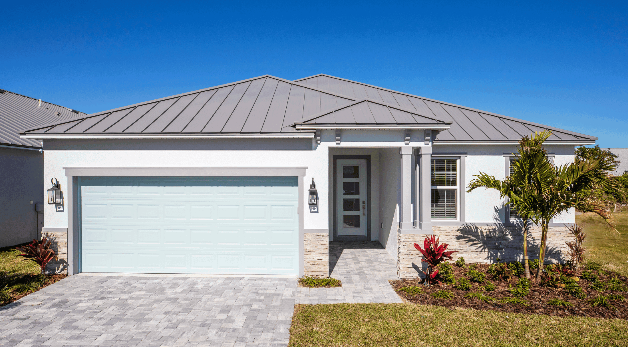 Modern single-story white house with a metal roof, landscaped front yard, and a double garage.