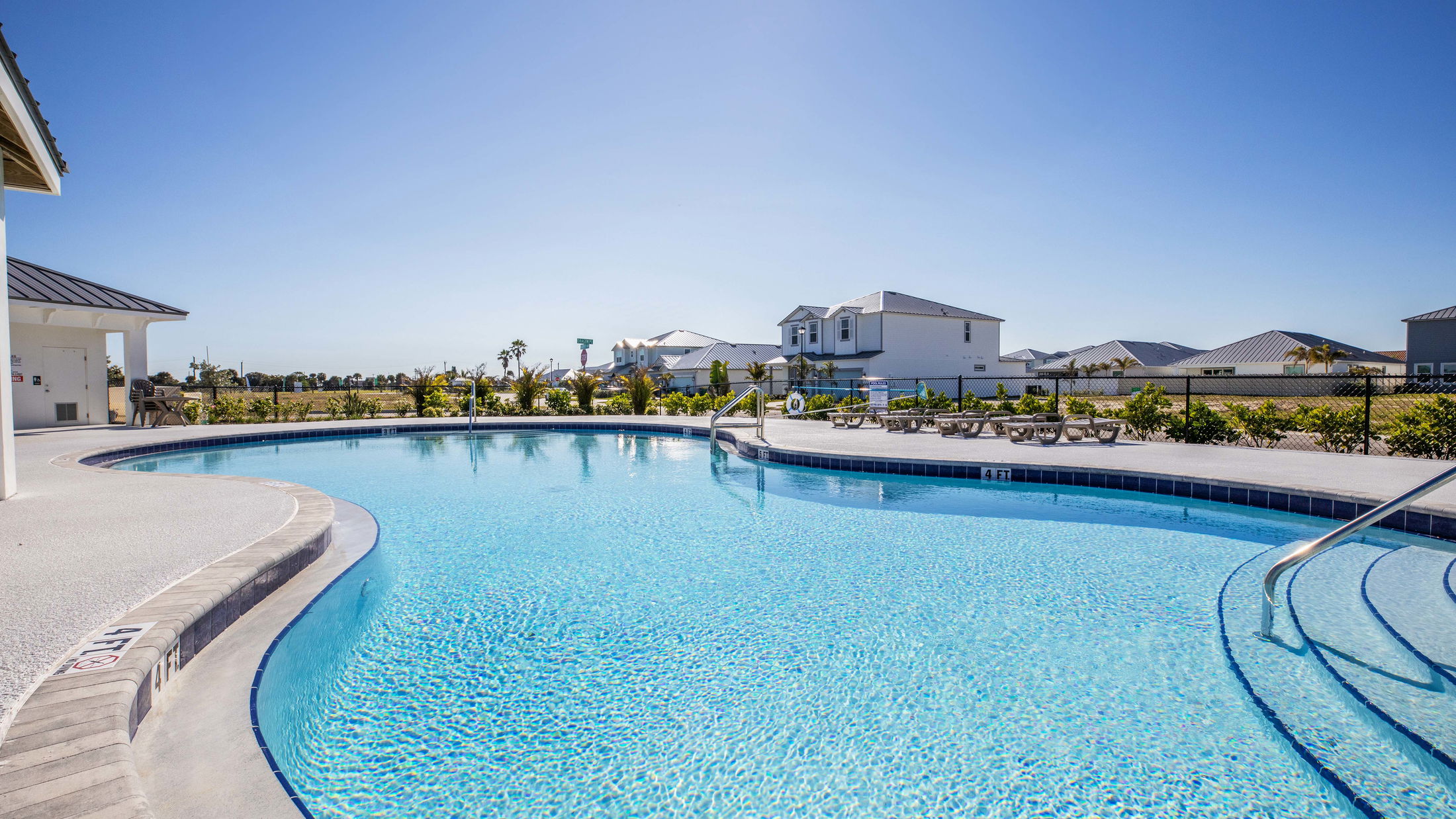 Sparkling blue swimming pool in sunny residential neighborhood with lounge chairs and clear skies.