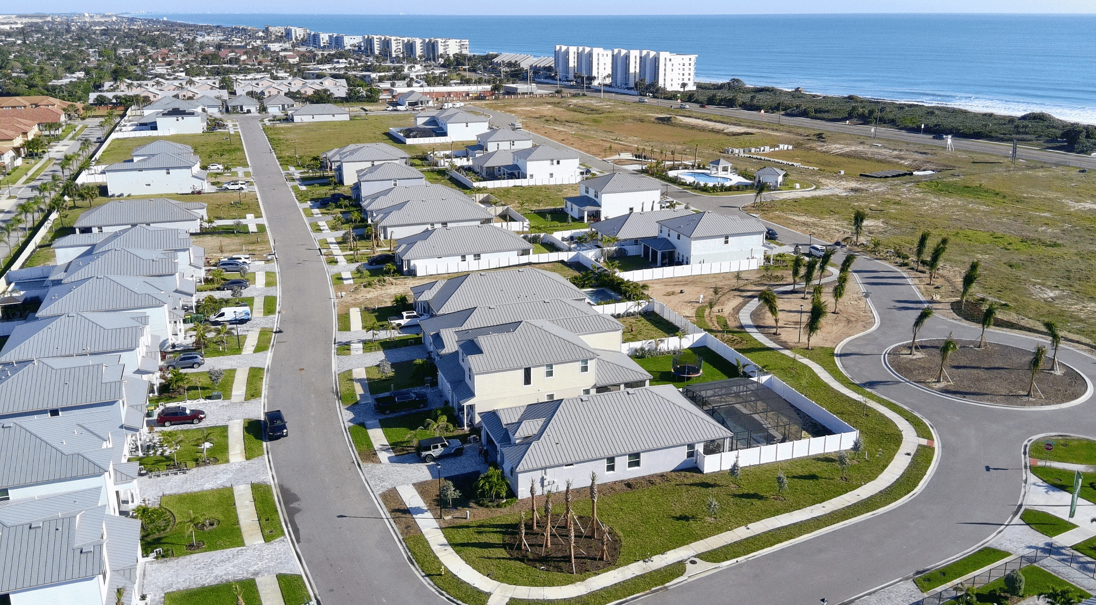 Aerial view of a modern coastal residential neighborhood with homes and ocean in the background.