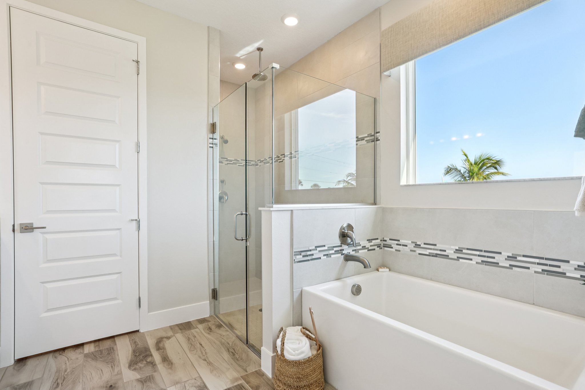 Modern bathroom featuring a glass-enclosed shower, large bathtub with tile accents, and a window with a scenic view.