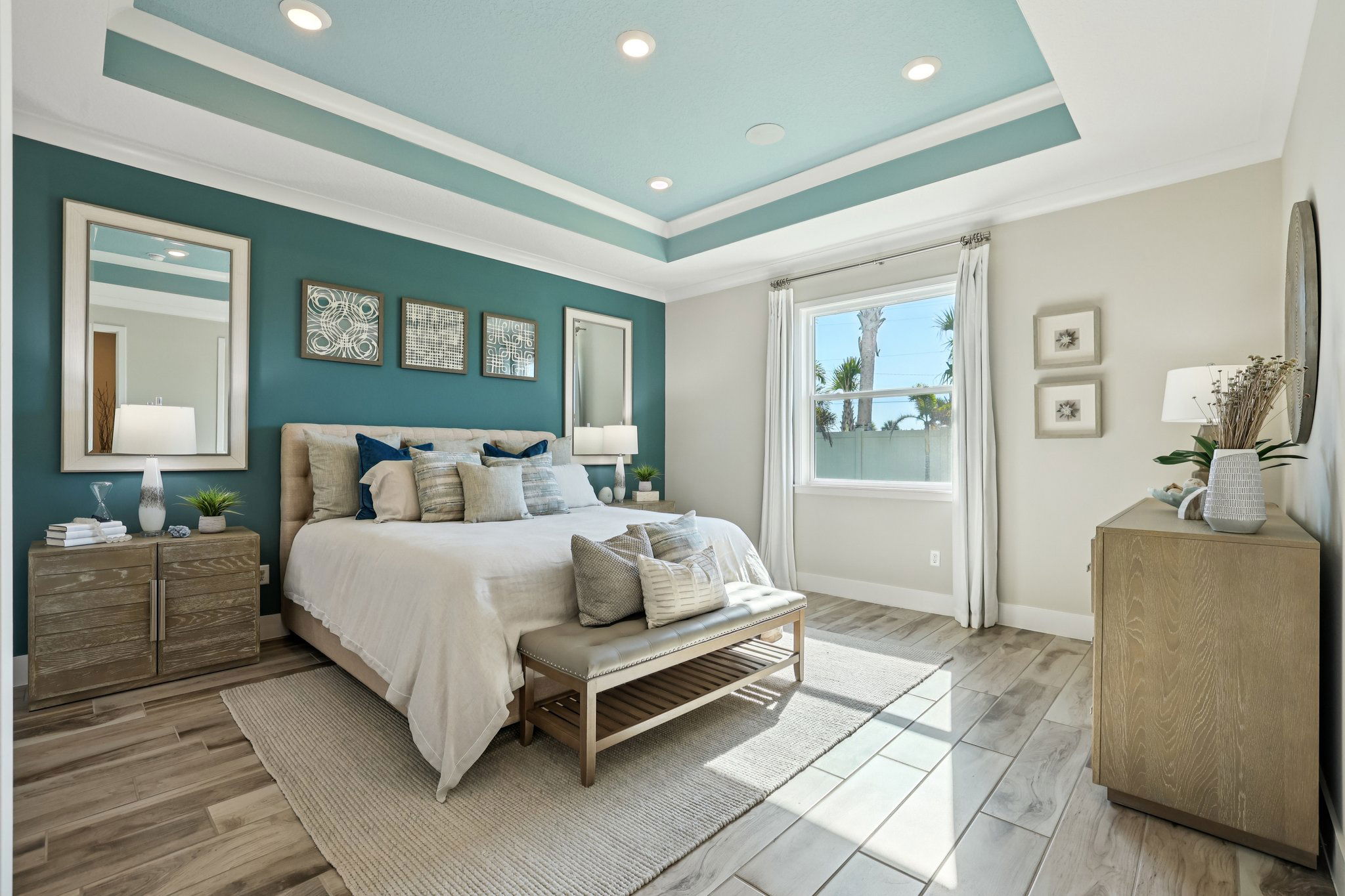 Modern bedroom with teal accent wall, stylish decor, and natural light streaming through a large window.