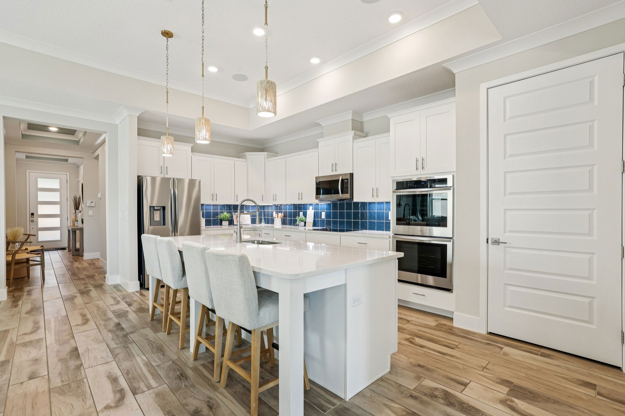 Modern kitchen with white cabinets, a central island with bar stools, stainless steel appliances, and blue tile backsplash.