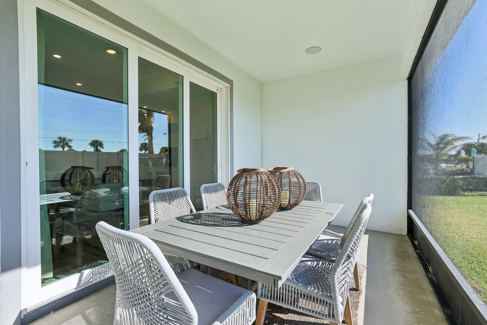 Modern outdoor patio with wicker chairs and a wooden dining table featuring decorative rattan lanterns.