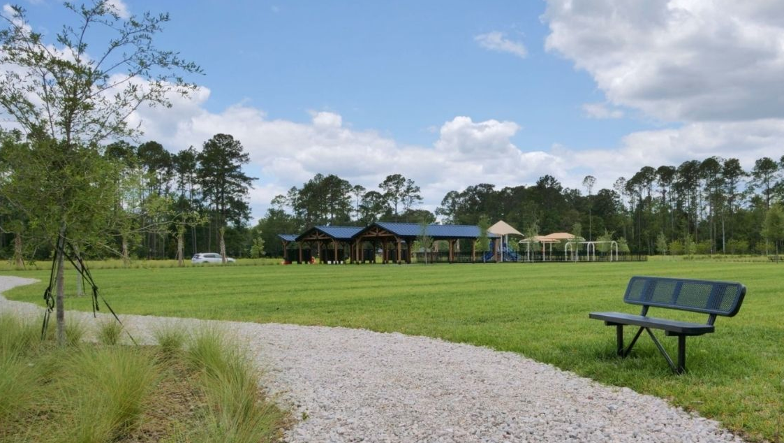 Park setting with a gravel path, a bench, and playground equipment under a blue sky.