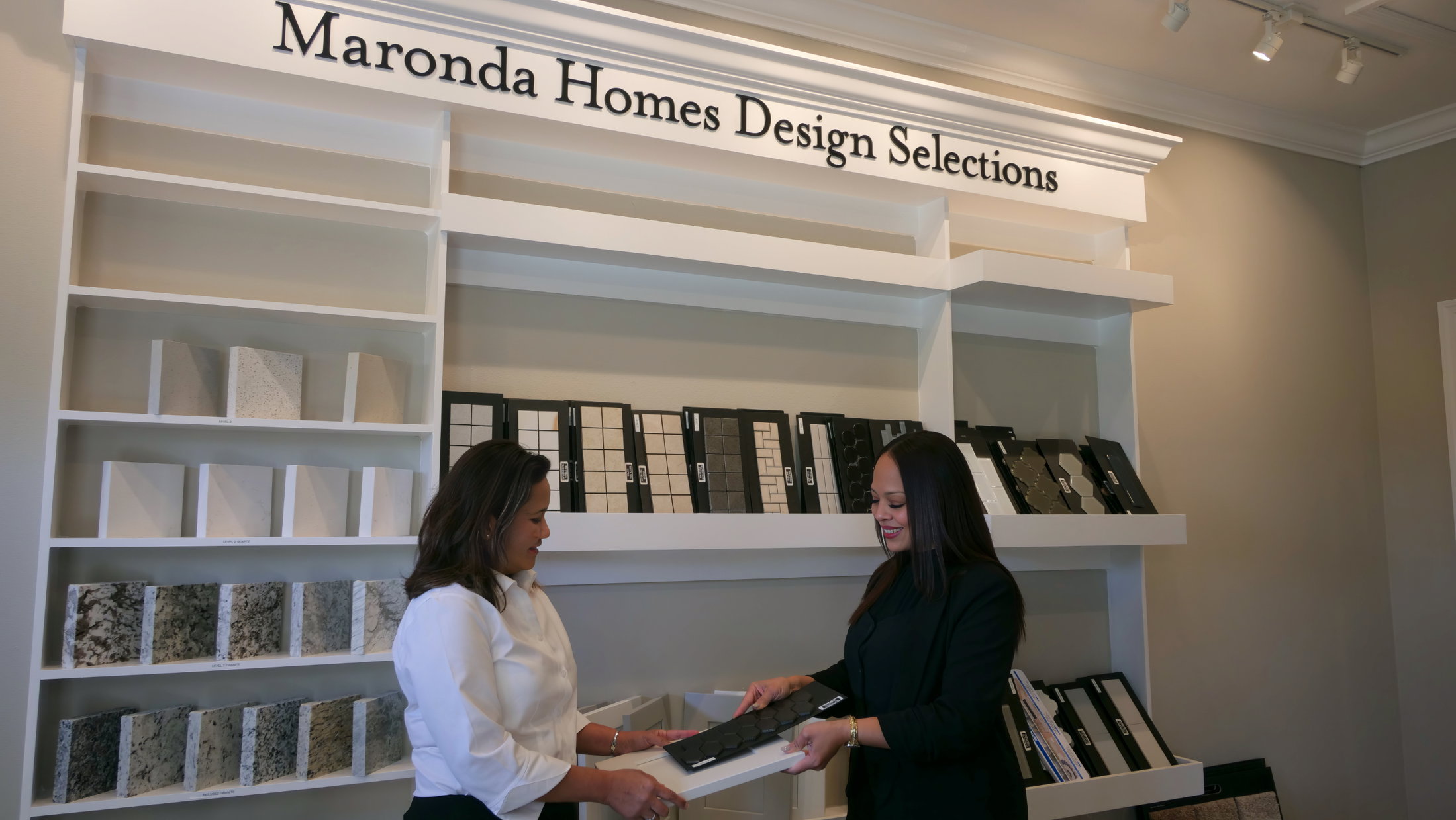 Two women are discussing design selections in a stylish showroom filled with various materials and samples.
