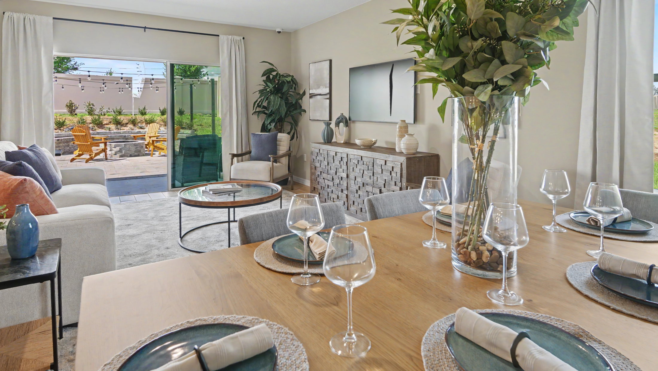 A dining table set with wine glasses and plates, overlooking a bright living area with a view of an outdoor patio.