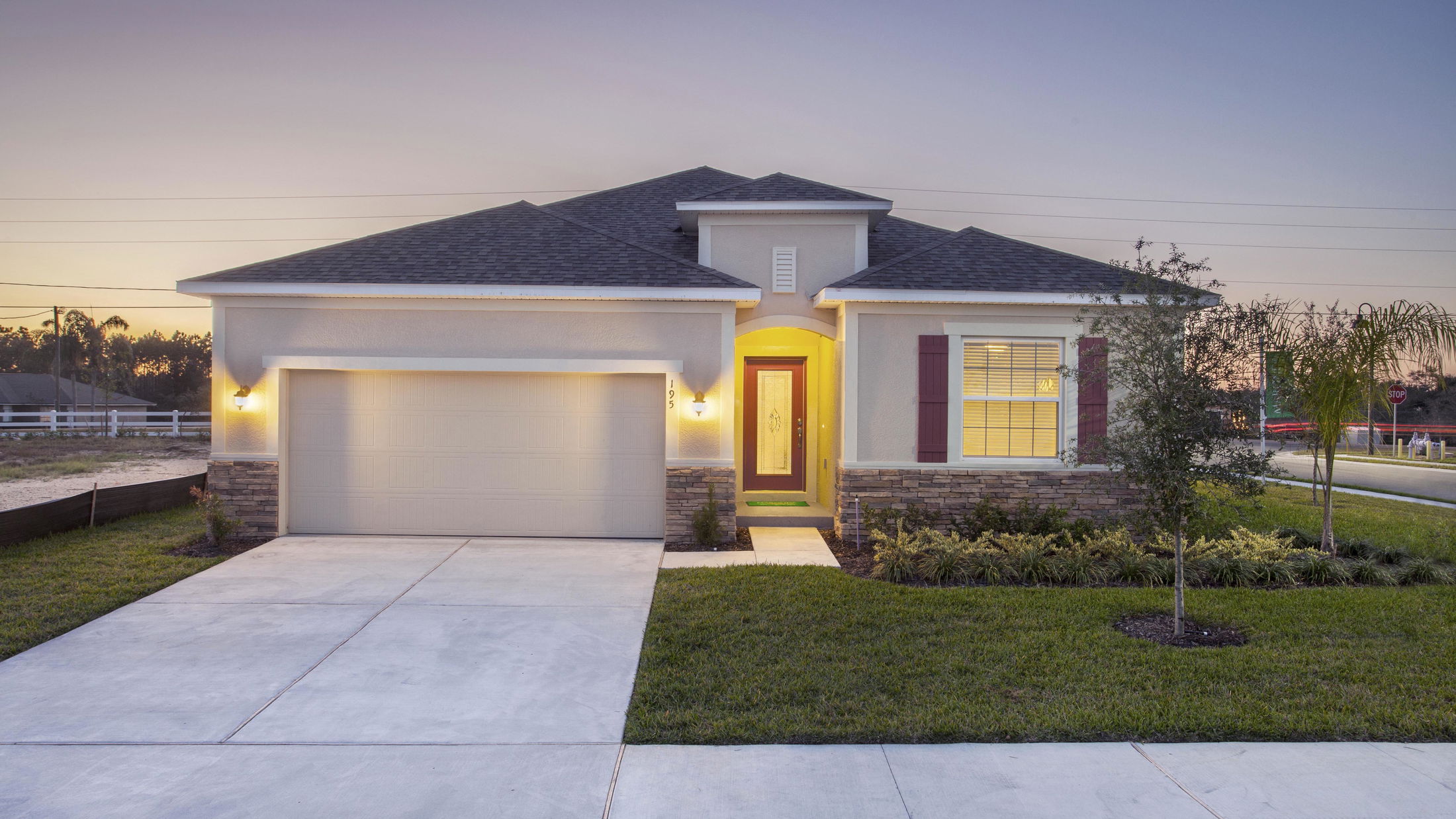 Modern suburban home with illuminated entrance, two-car garage, and well-maintained front lawn at dusk.