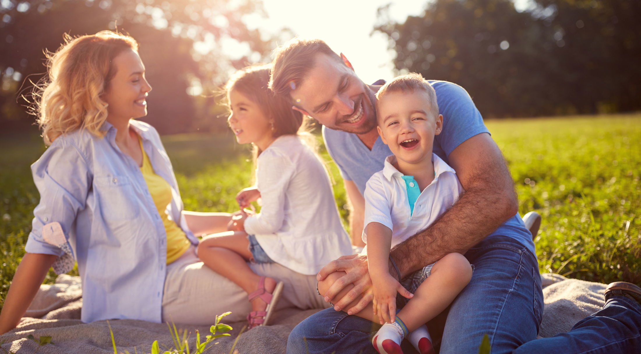 A joyful family enjoys a sunny day on a picnic blanket in a lush green park.