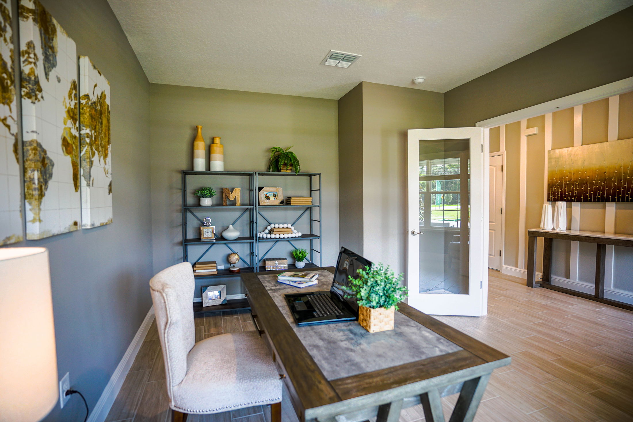 Modern home office with wooden desk, laptop, bookshelf, and stylish decor in a well-lit room.