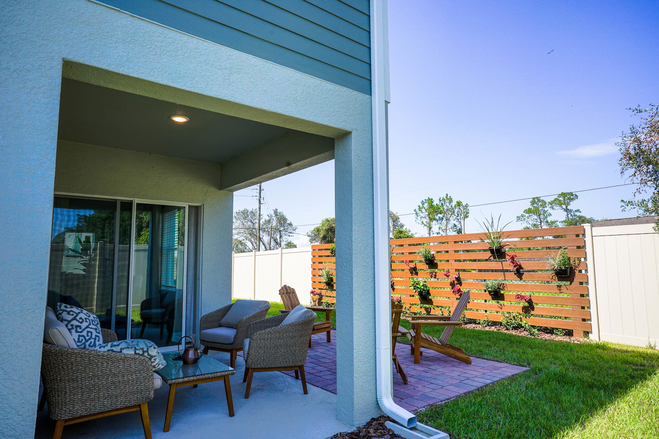 Modern patio with wicker furniture and a vertical garden on a wooden fence in a sunny backyard.