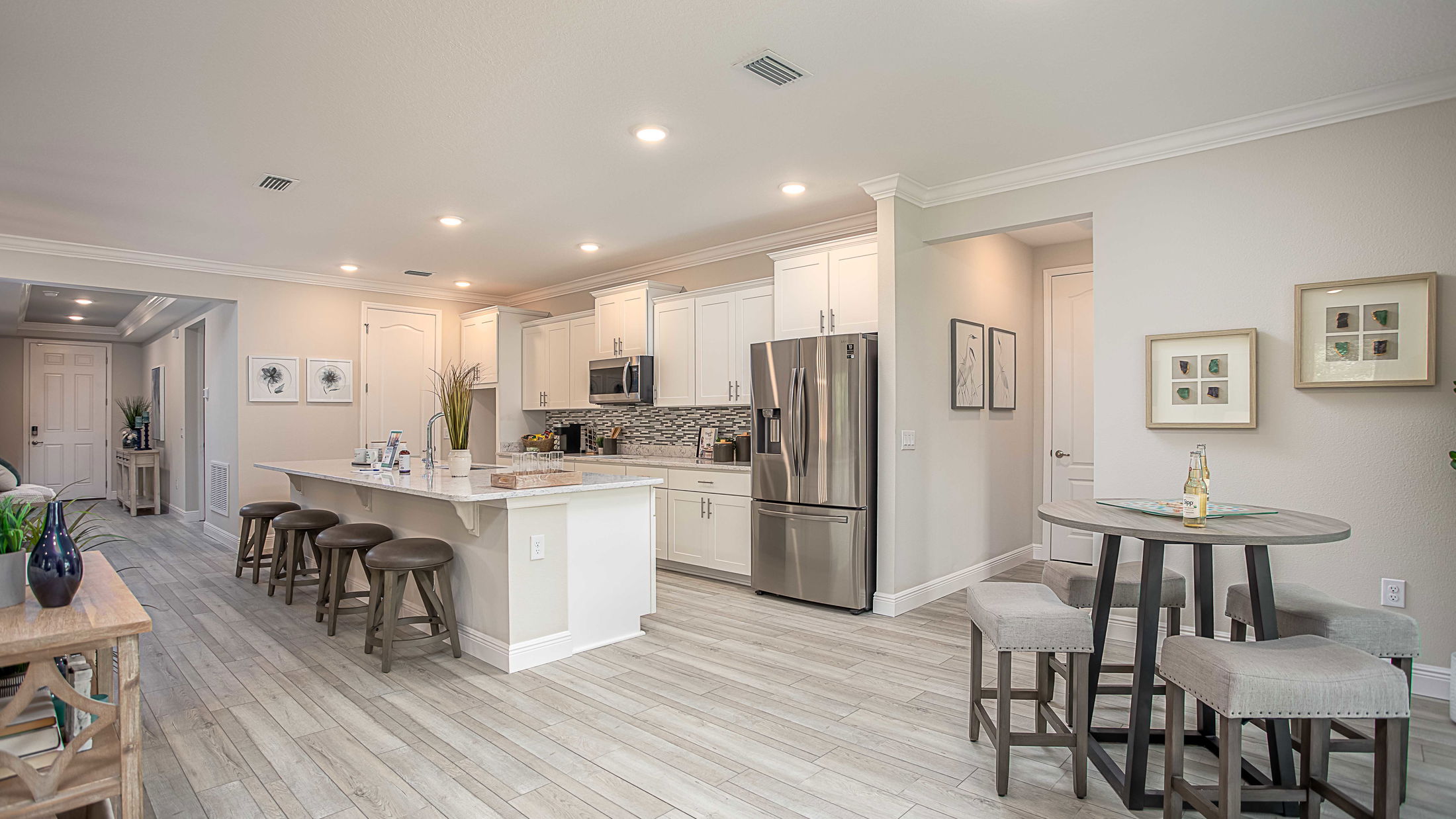 Modern kitchen interior with white cabinets, a large island with stools, and a stainless steel refrigerator.