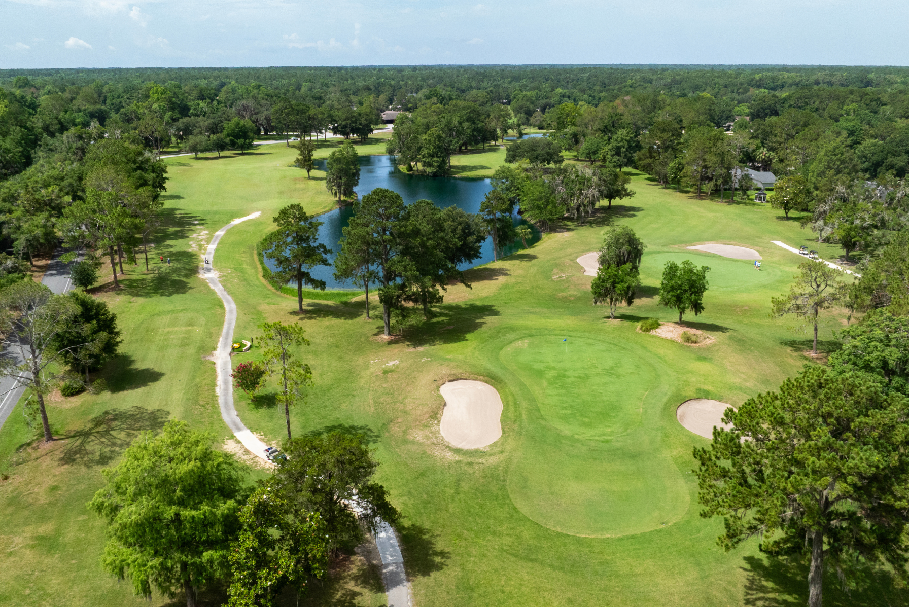 Aerial view of a scenic golf course featuring lush greens, sand bunkers, winding paths, and a picturesque pond surrounded by trees.