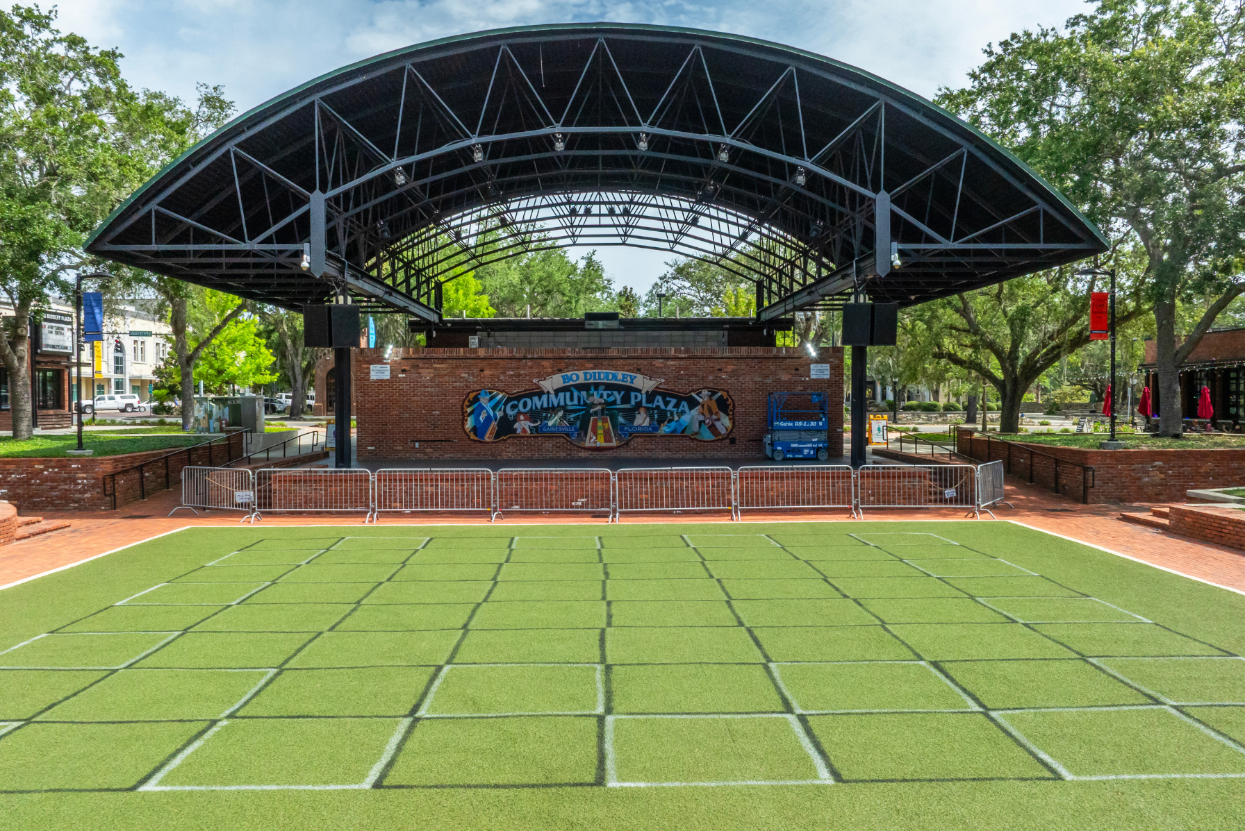 Outdoor stage at Bo Diddley Community Plaza with green turf and surrounding trees in Gainesville, Florida.