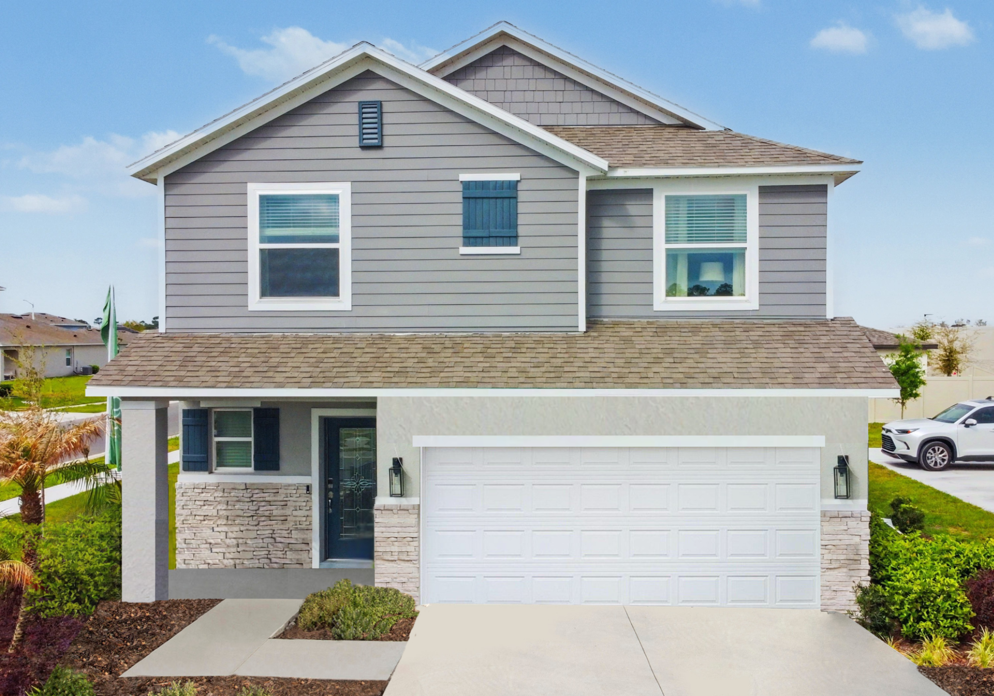 Two-story gray house with a stone-accented facade, a two-car garage, and green landscaping.