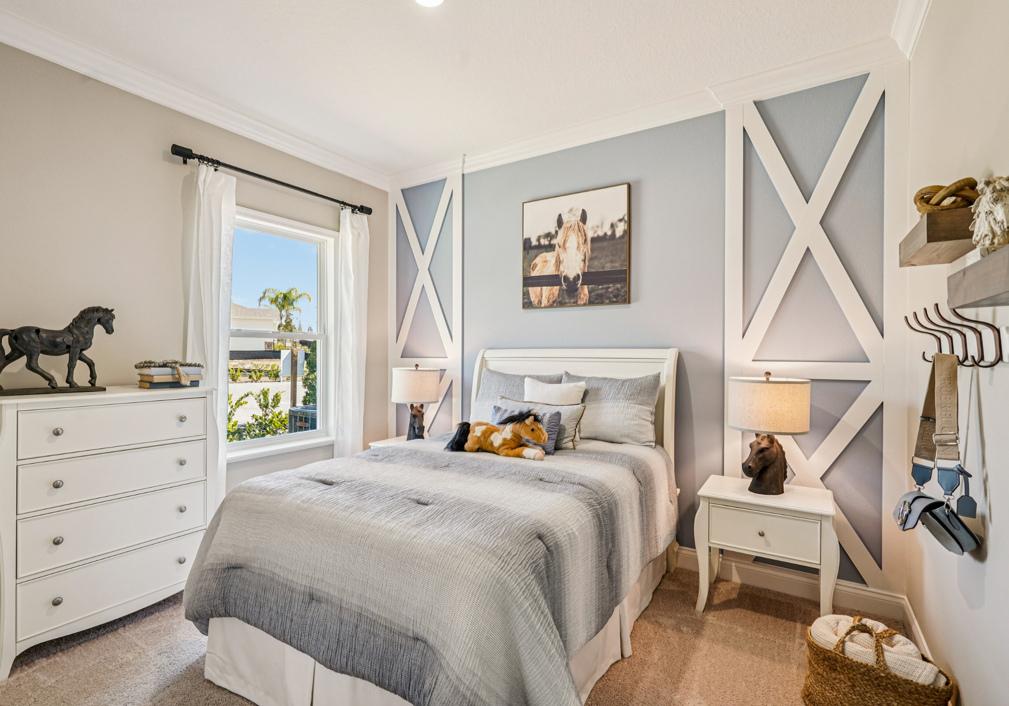 Cozy bedroom featuring a bed with gray bedding, a nightstand with a lamp, a dresser, and wall art, all in a light color palette.