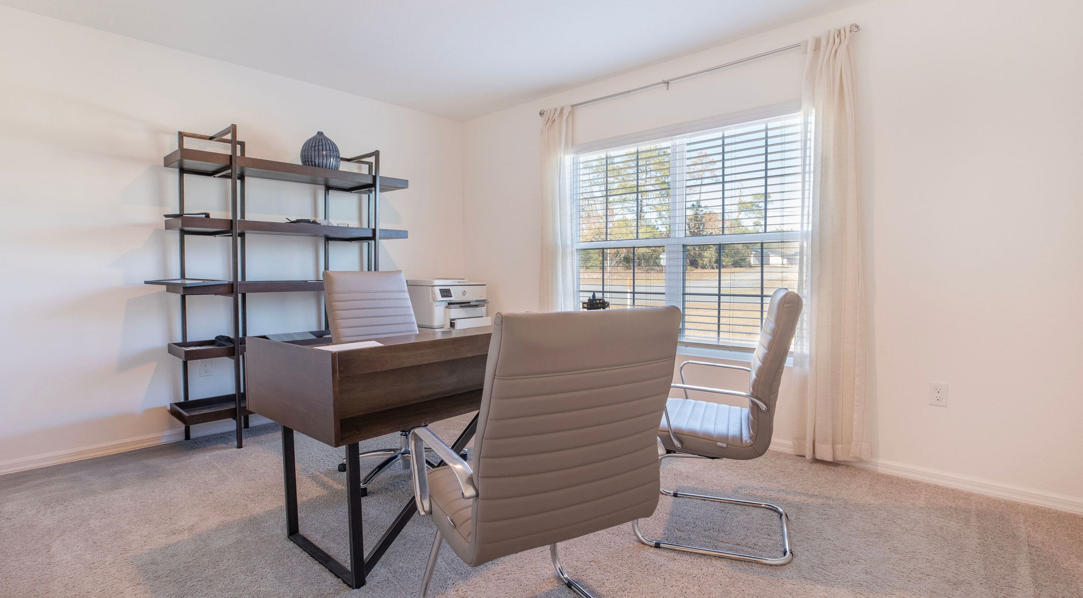 Bright and modern home office with a wooden desk, stylish shelving, and beige leather chairs by a large window.