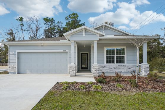 A modern single-story home with a light blue exterior, stone accents, and a well-landscaped yard.